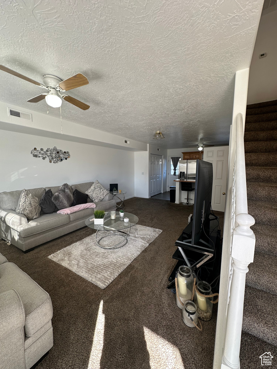 Living room with ceiling fan, carpet floors, and a textured ceiling