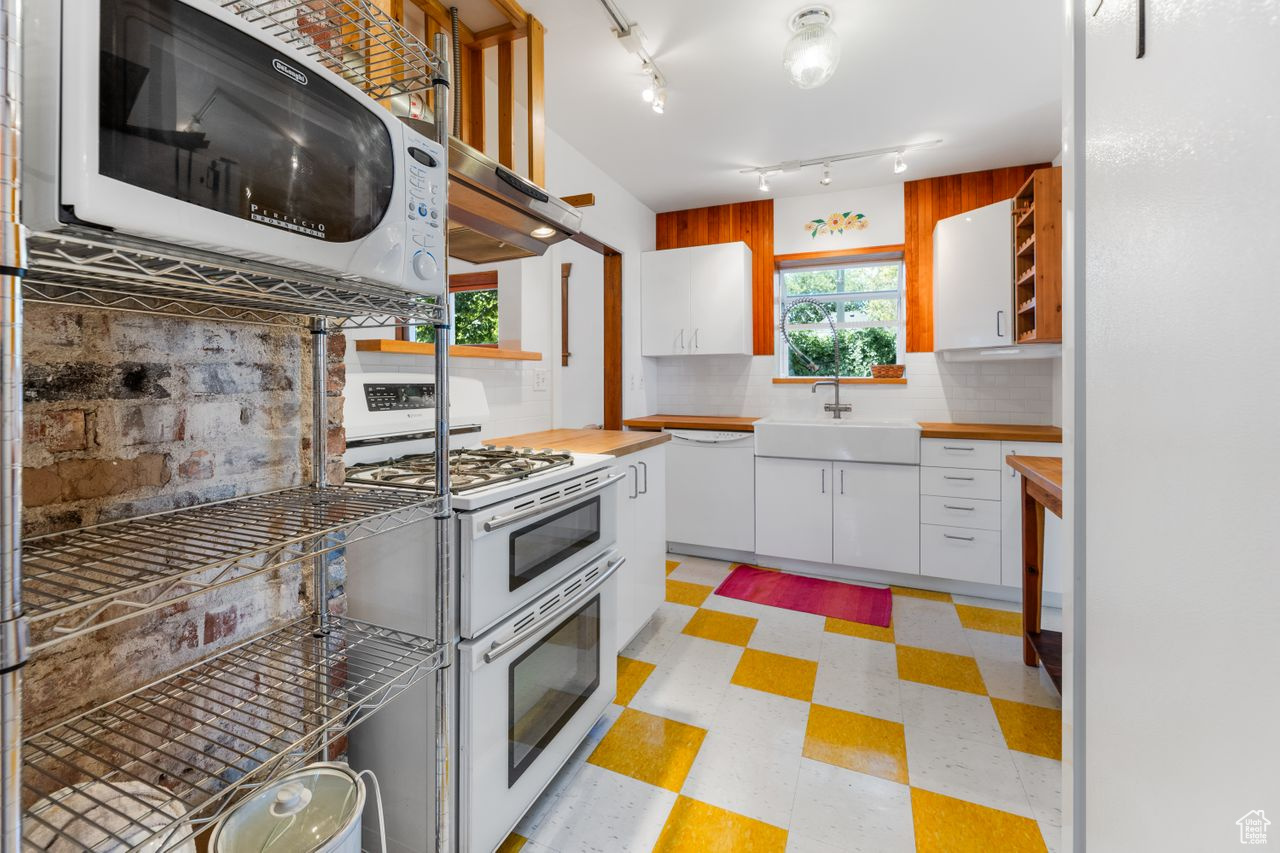 Kitchen featuring backsplash, white appliances, sink, and white cabinets