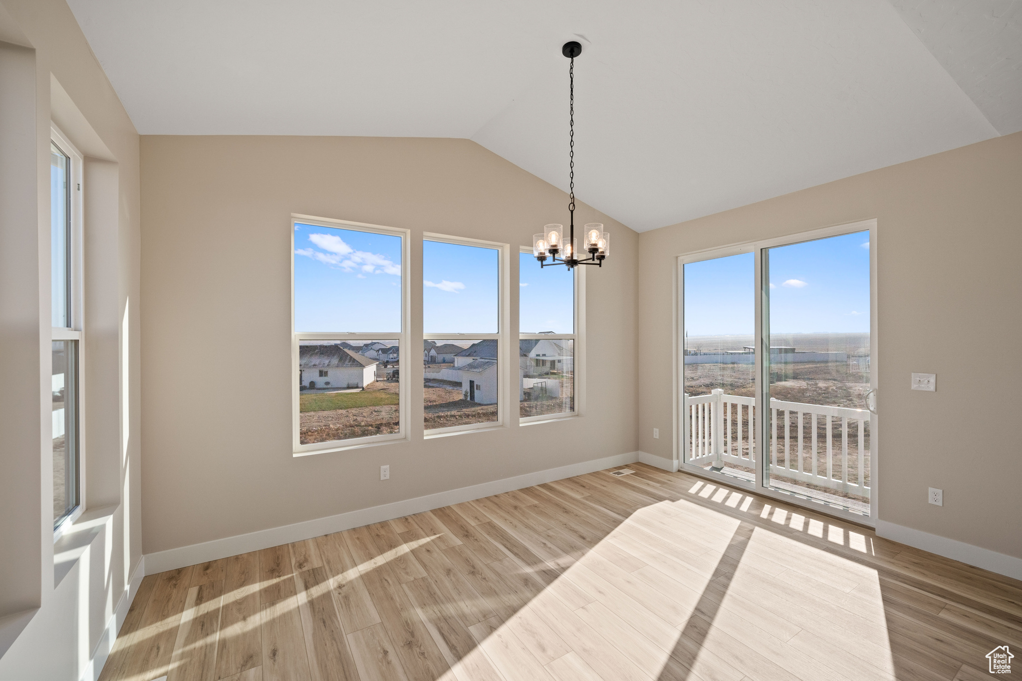 Unfurnished dining area featuring vaulted ceiling, light wood-type flooring, and an inviting chandelier