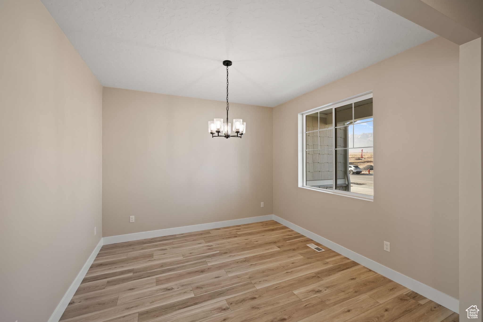 Empty room featuring a notable chandelier and light hardwood / wood-style flooring