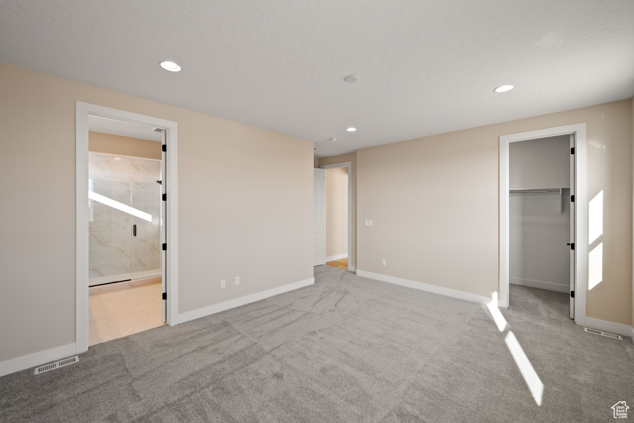 Unfurnished bedroom featuring ensuite bathroom, a spacious closet, light colored carpet, and a closet