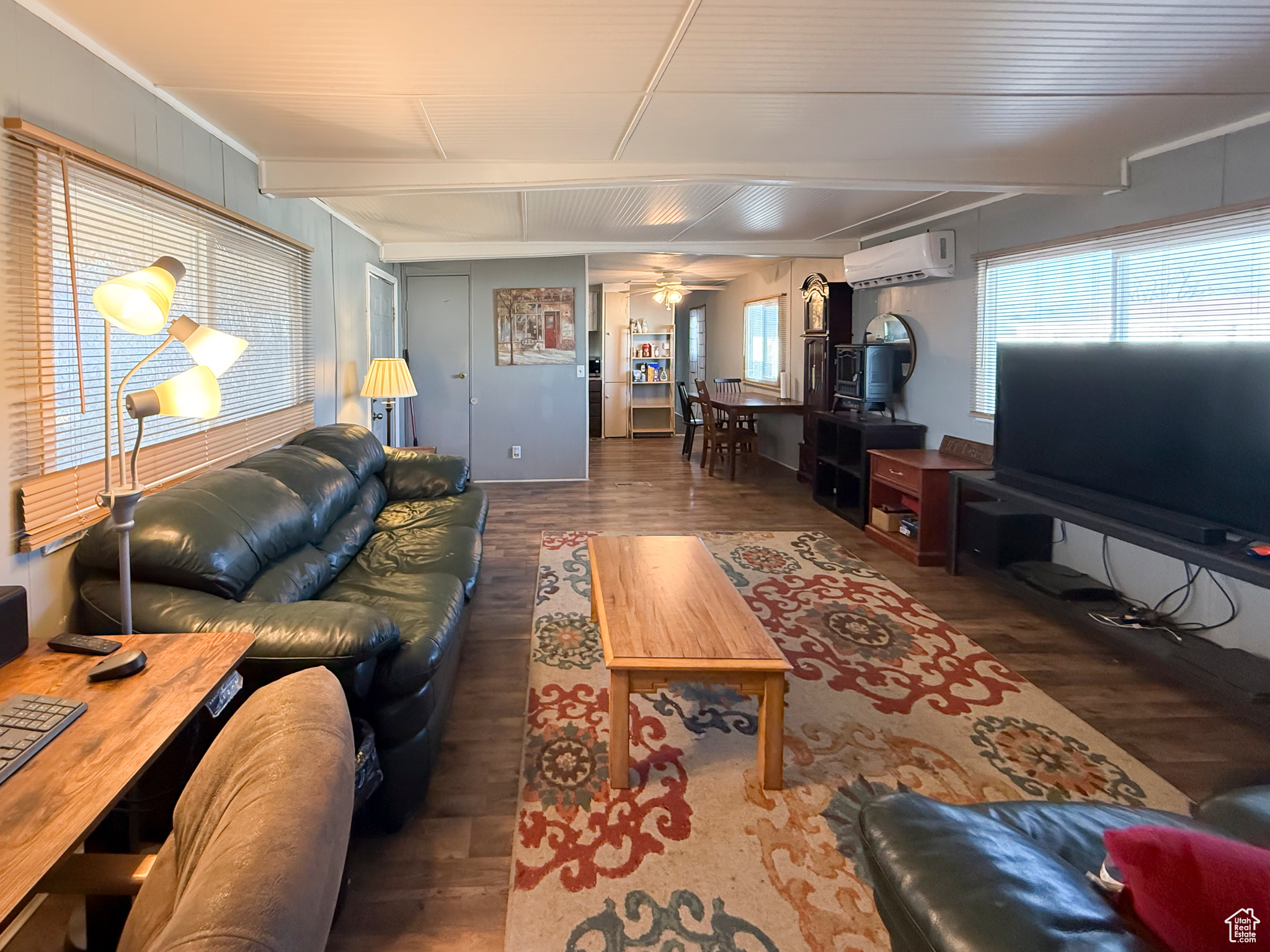 Living room with dark wood-type flooring, ceiling fan, beam ceiling, and an AC wall unit