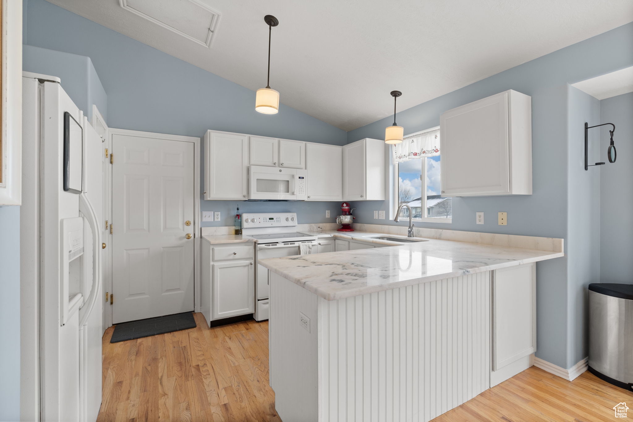 Kitchen with sink, white cabinets, hanging light fixtures, kitchen peninsula, and white appliances