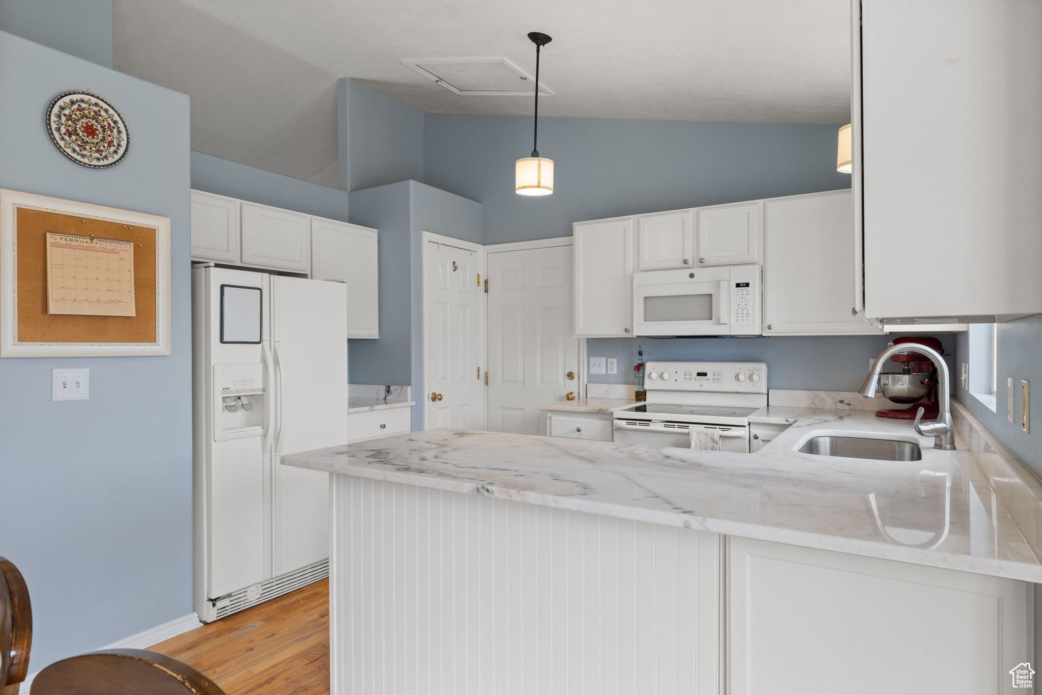 Kitchen with white appliances, kitchen peninsula, hanging light fixtures, and white cabinets