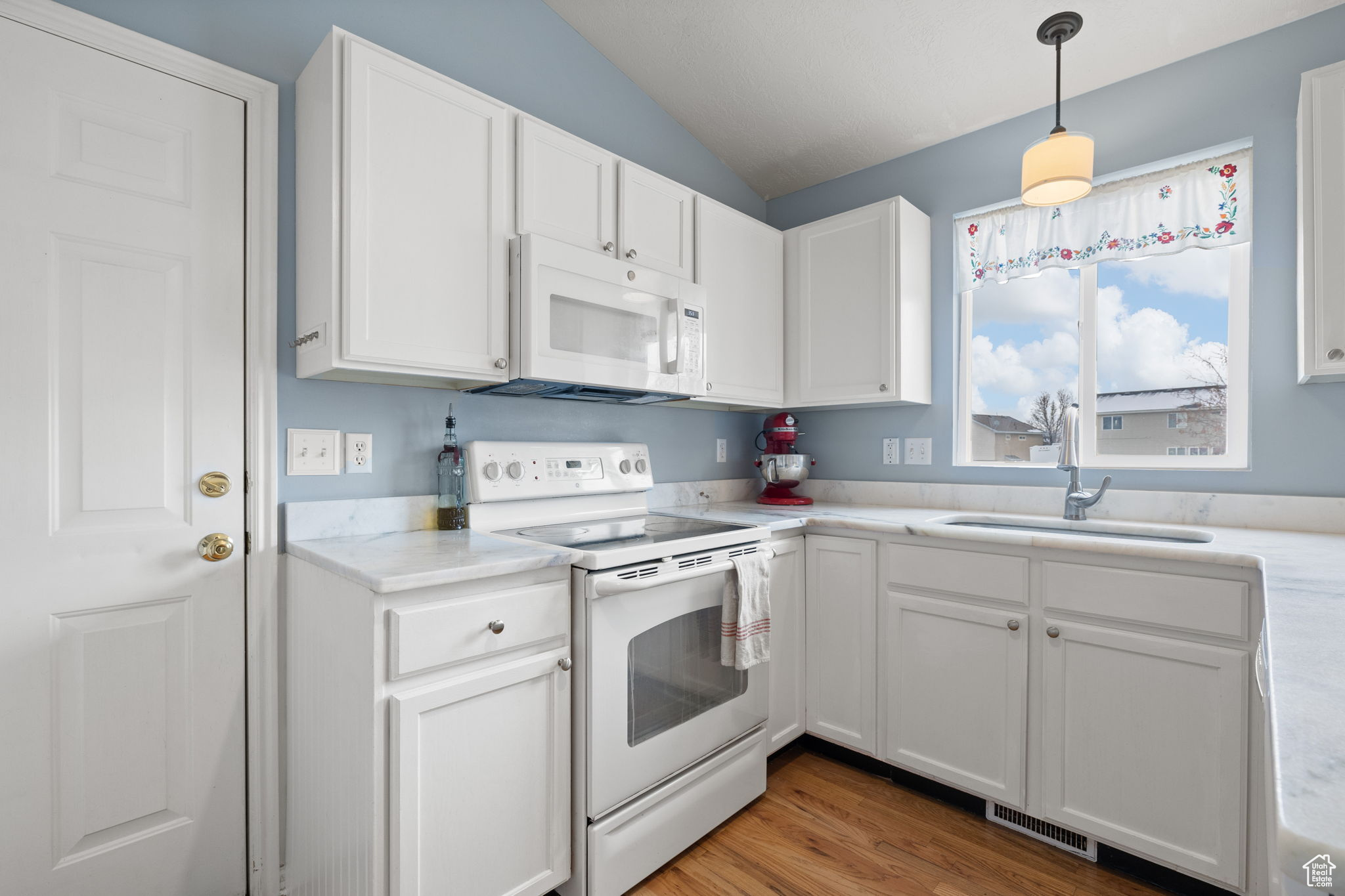 Kitchen featuring white cabinetry, white appliances, sink, and hanging light fixtures