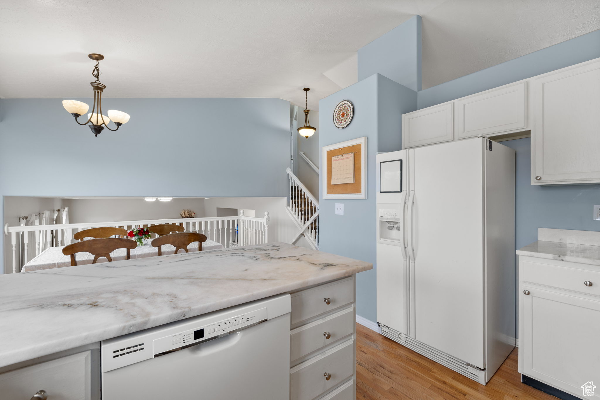 Kitchen featuring white appliances, light hardwood / wood-style flooring, white cabinetry, hanging light fixtures, and a notable chandelier