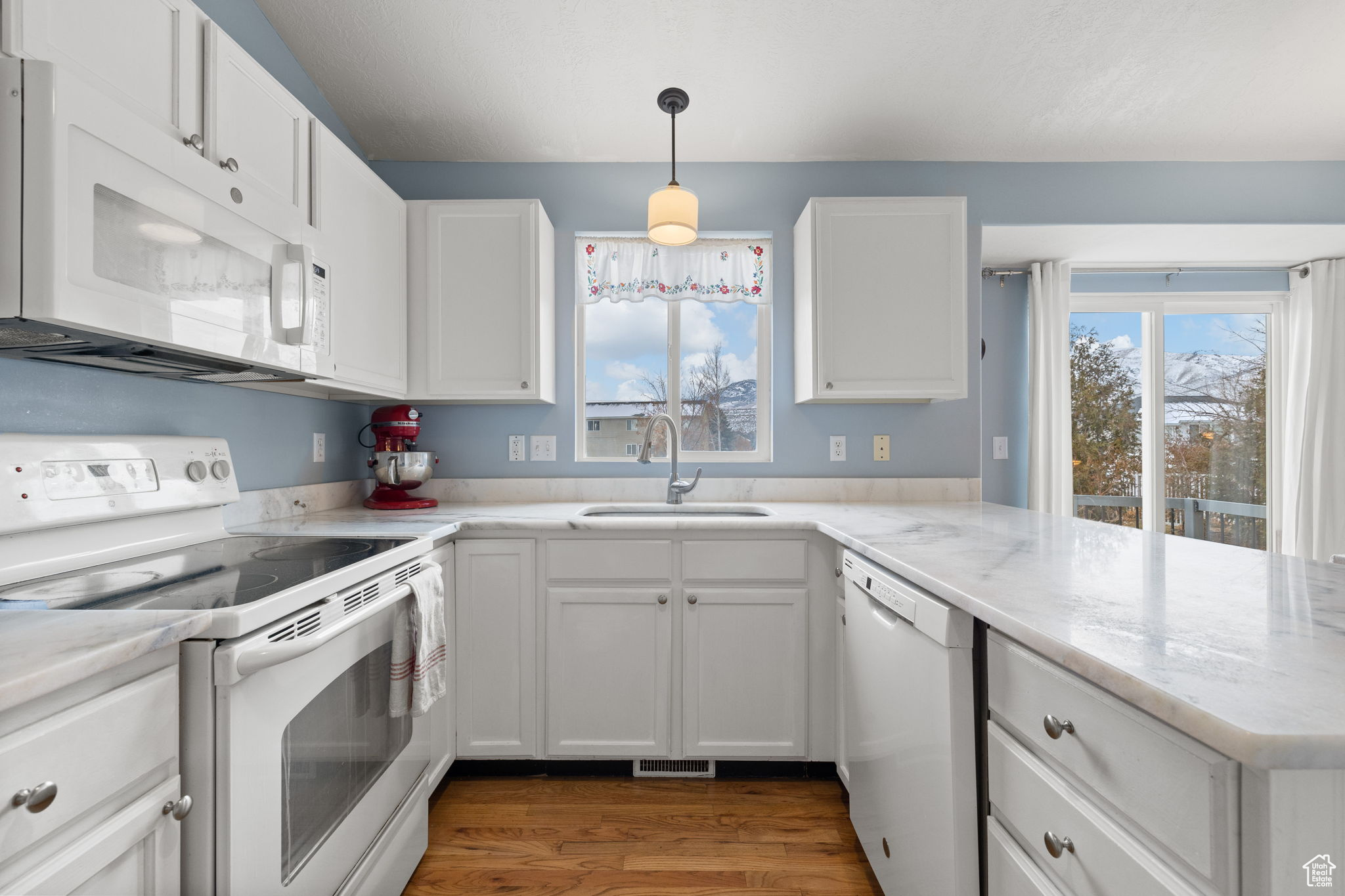 Kitchen featuring sink, hanging light fixtures, kitchen peninsula, white appliances, and white cabinets