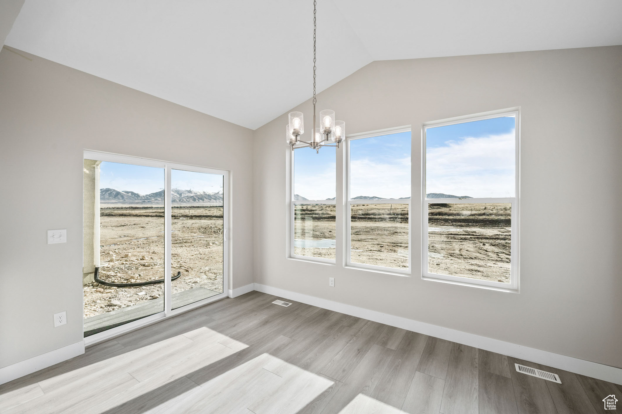 Unfurnished dining area with a notable chandelier, lofted ceiling, a mountain view, and light wood-type flooring