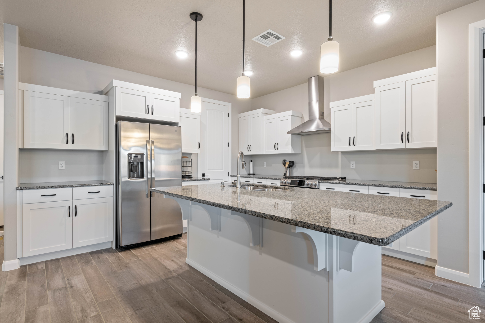 Kitchen featuring white cabinetry, pendant lighting, stainless steel fridge, and wall chimney range hood