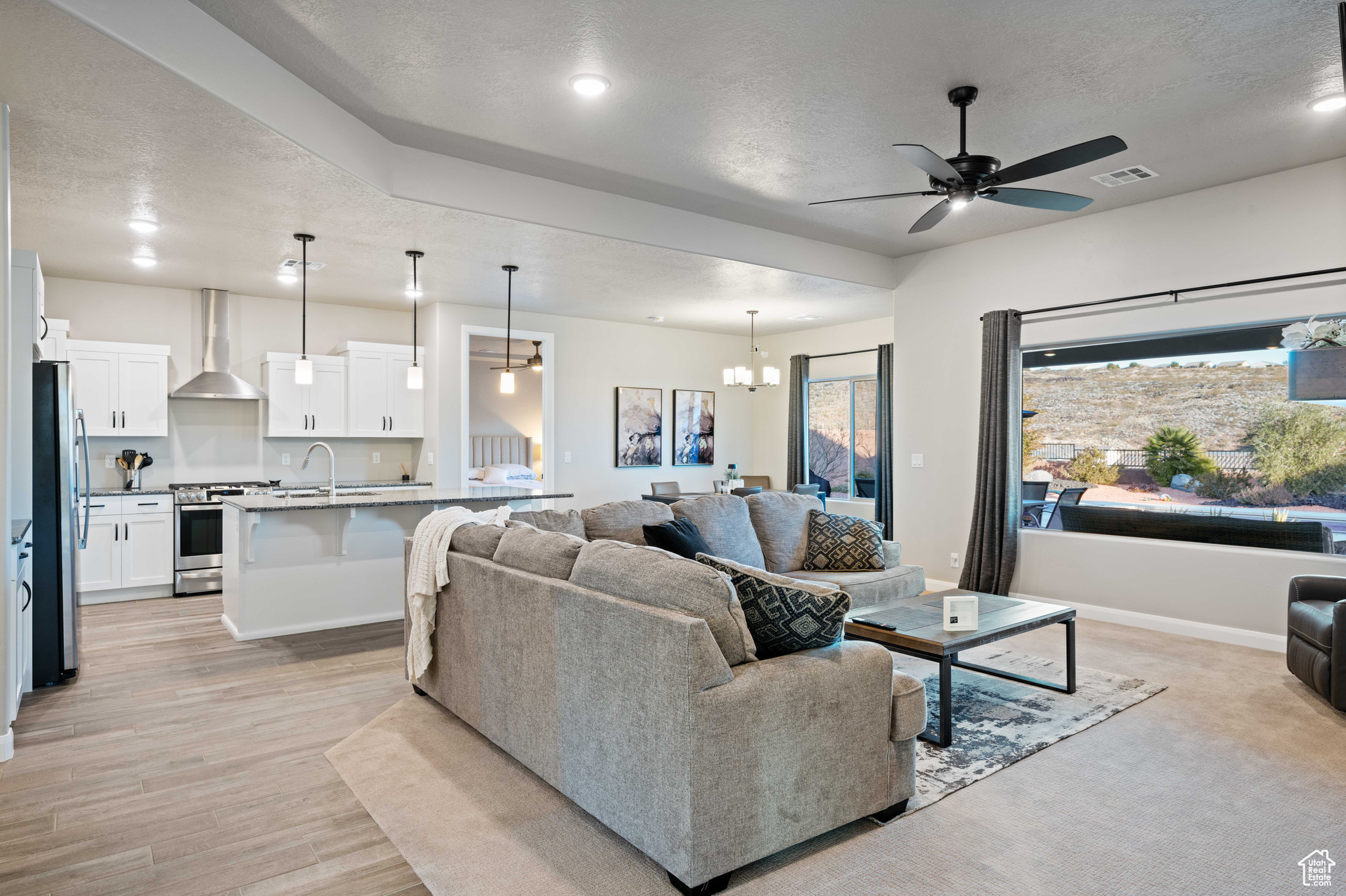 Living room with ceiling fan with notable chandelier, light hardwood / wood-style flooring, and a textured ceiling