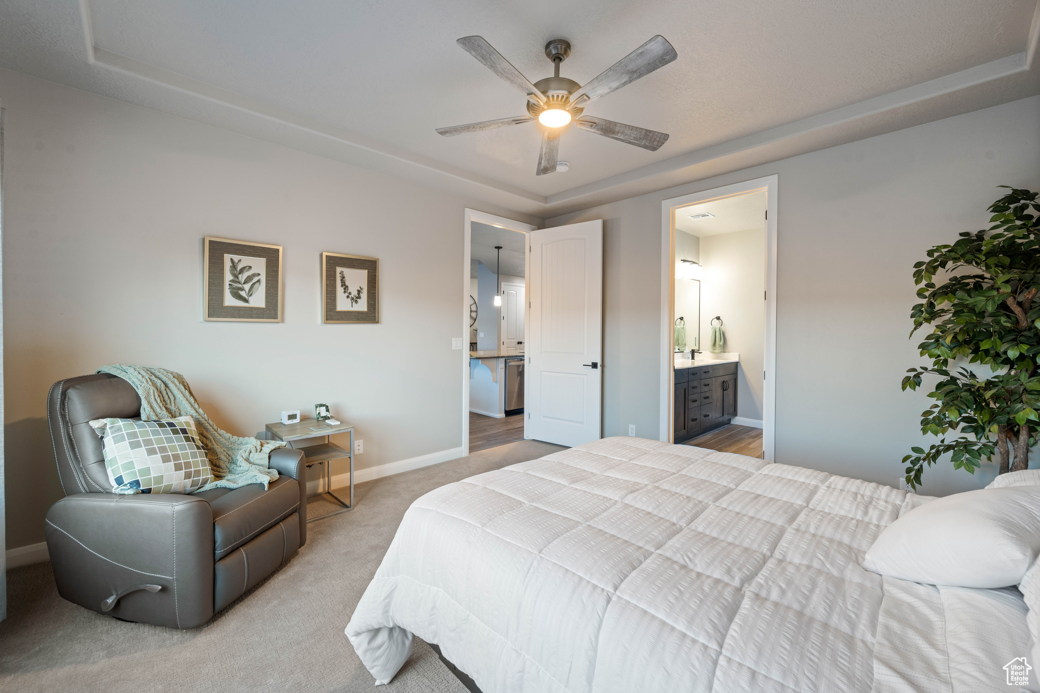 Bedroom with light carpet, connected bathroom, a raised ceiling, and ceiling fan