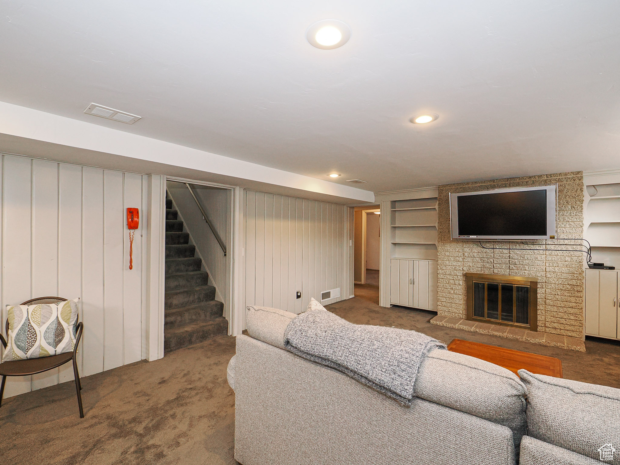 Living room with built in shelves, wooden walls, carpet flooring, and a brick fireplace