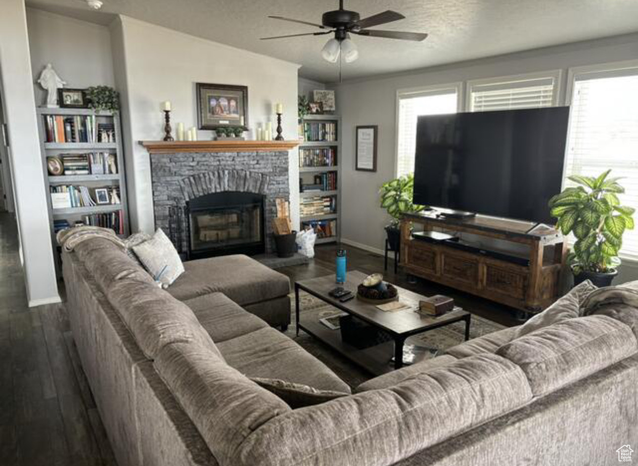 Living room with dark wood-type flooring, ceiling fan, a stone fireplace, and a textured ceiling