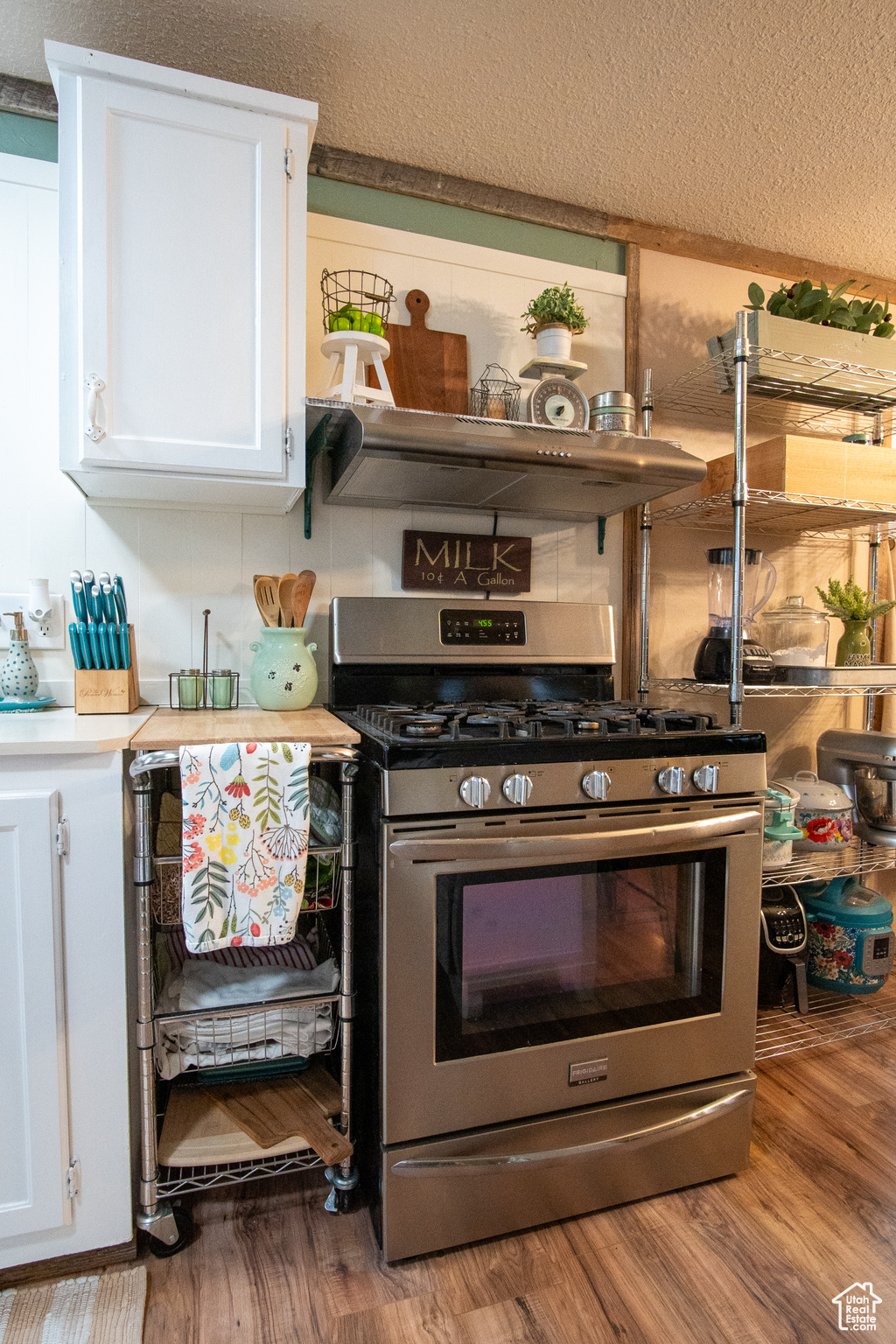 Kitchen featuring a textured ceiling, white cabinets, light hardwood / wood-style floors, and stainless steel gas stove