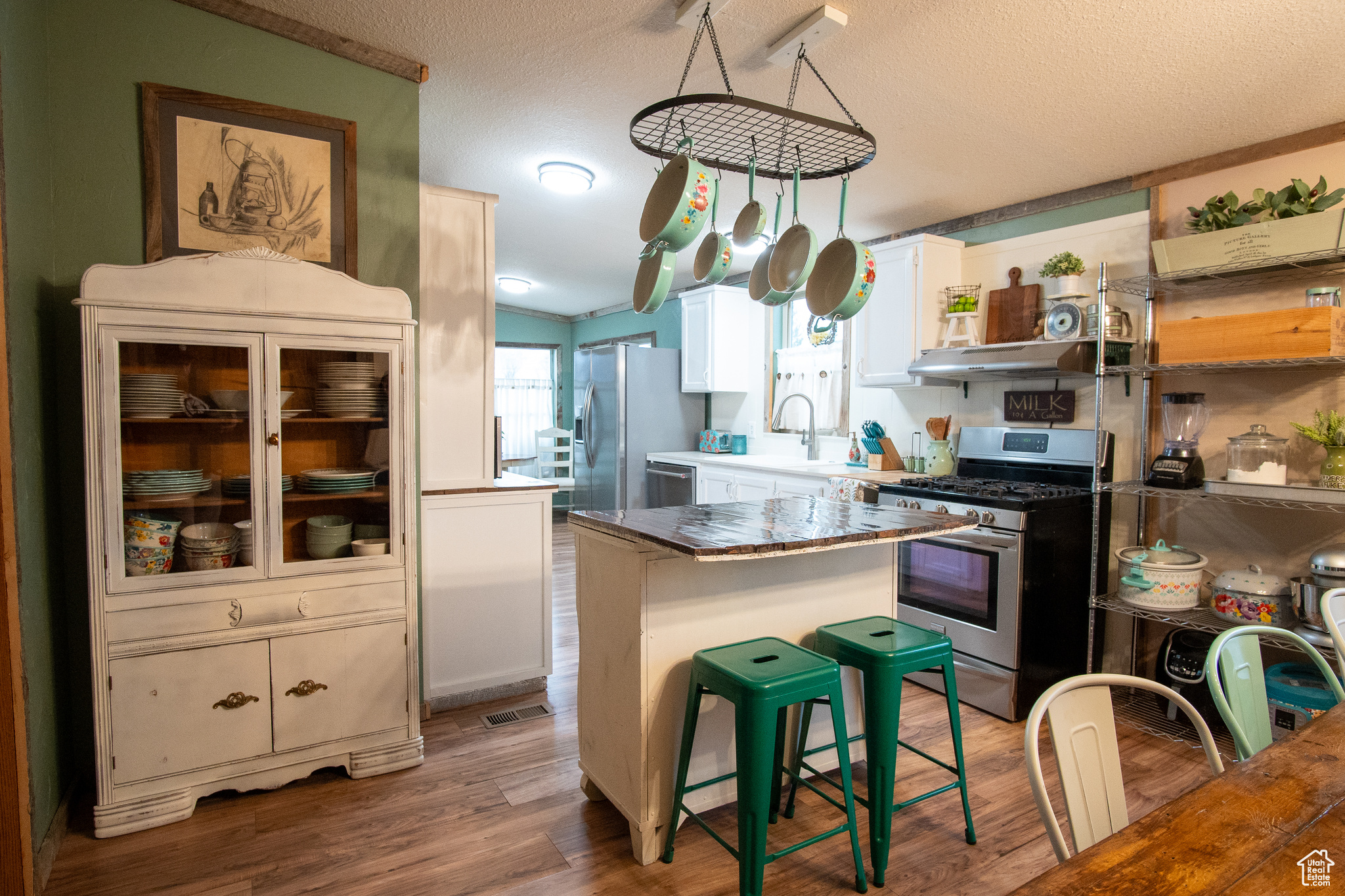 Kitchen with a breakfast bar area, appliances with stainless steel finishes, hardwood / wood-style floors, a textured ceiling, and white cabinets