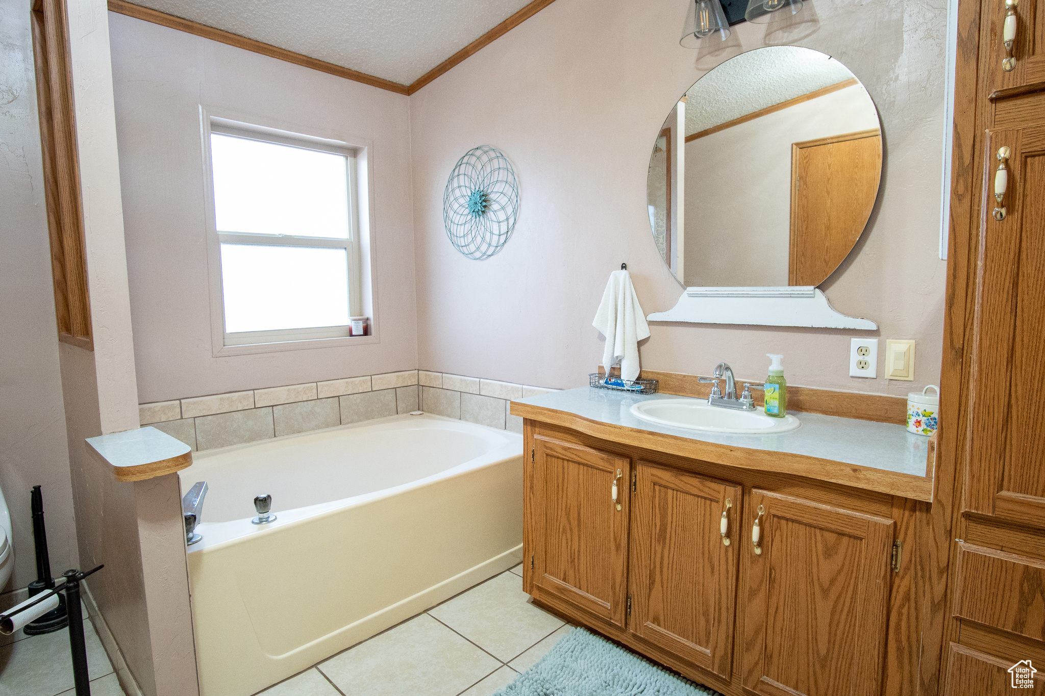 Bathroom with a tub to relax in, tile patterned flooring, ornamental molding, vanity, and a textured ceiling