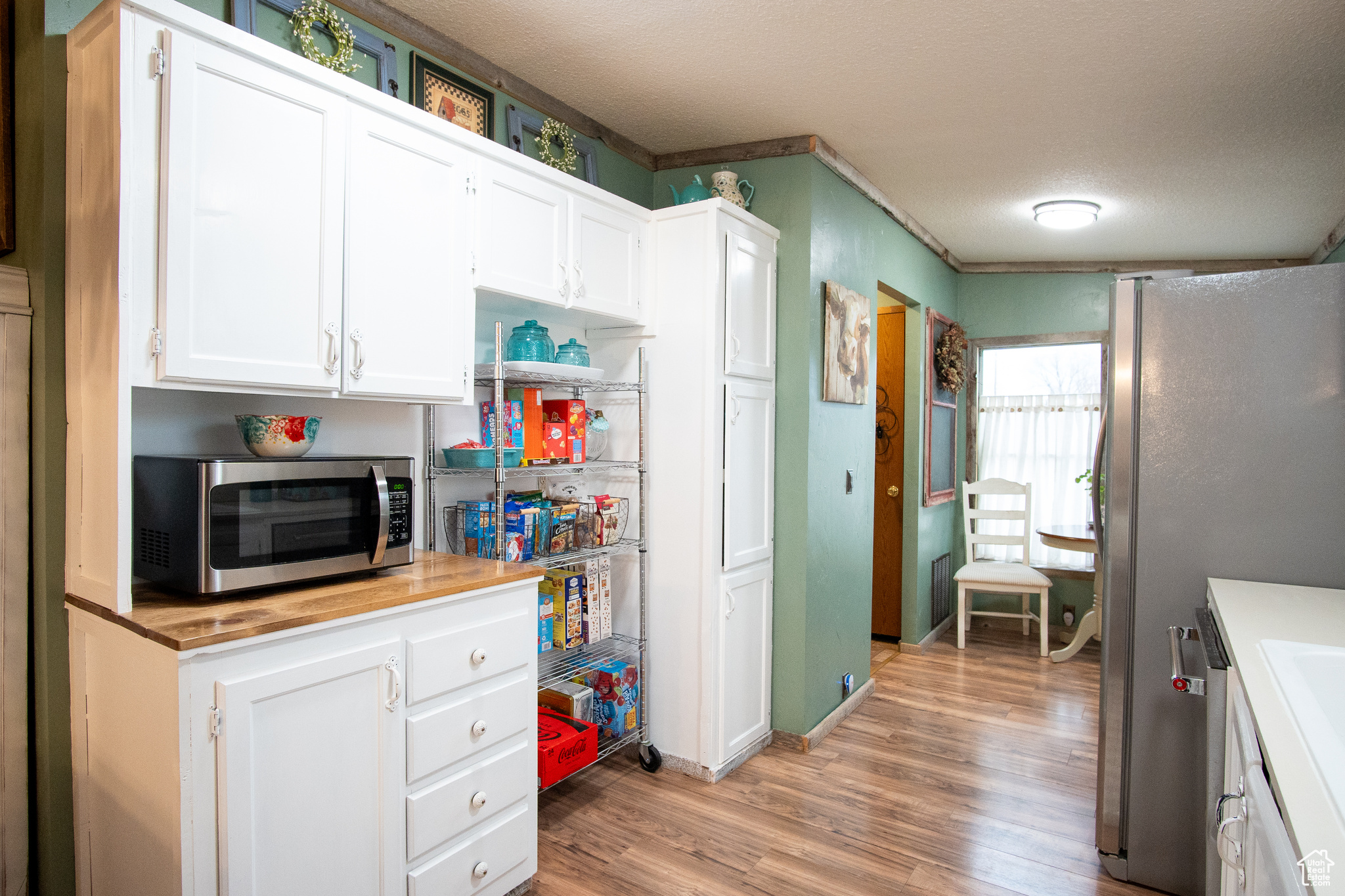 Kitchen with white cabinetry, stainless steel appliances, light hardwood / wood-style floors, and a textured ceiling