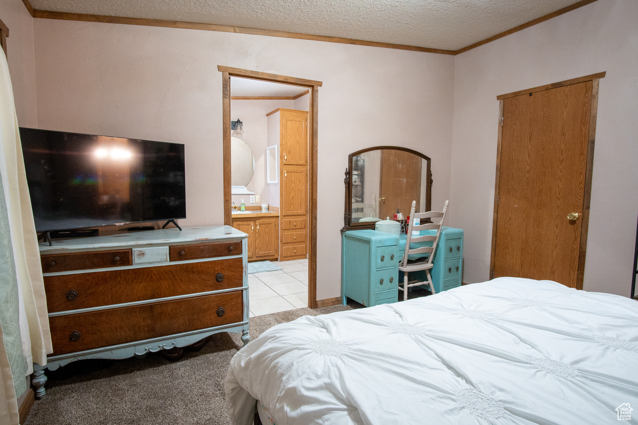 Carpeted bedroom featuring crown molding, ensuite bathroom, and a textured ceiling