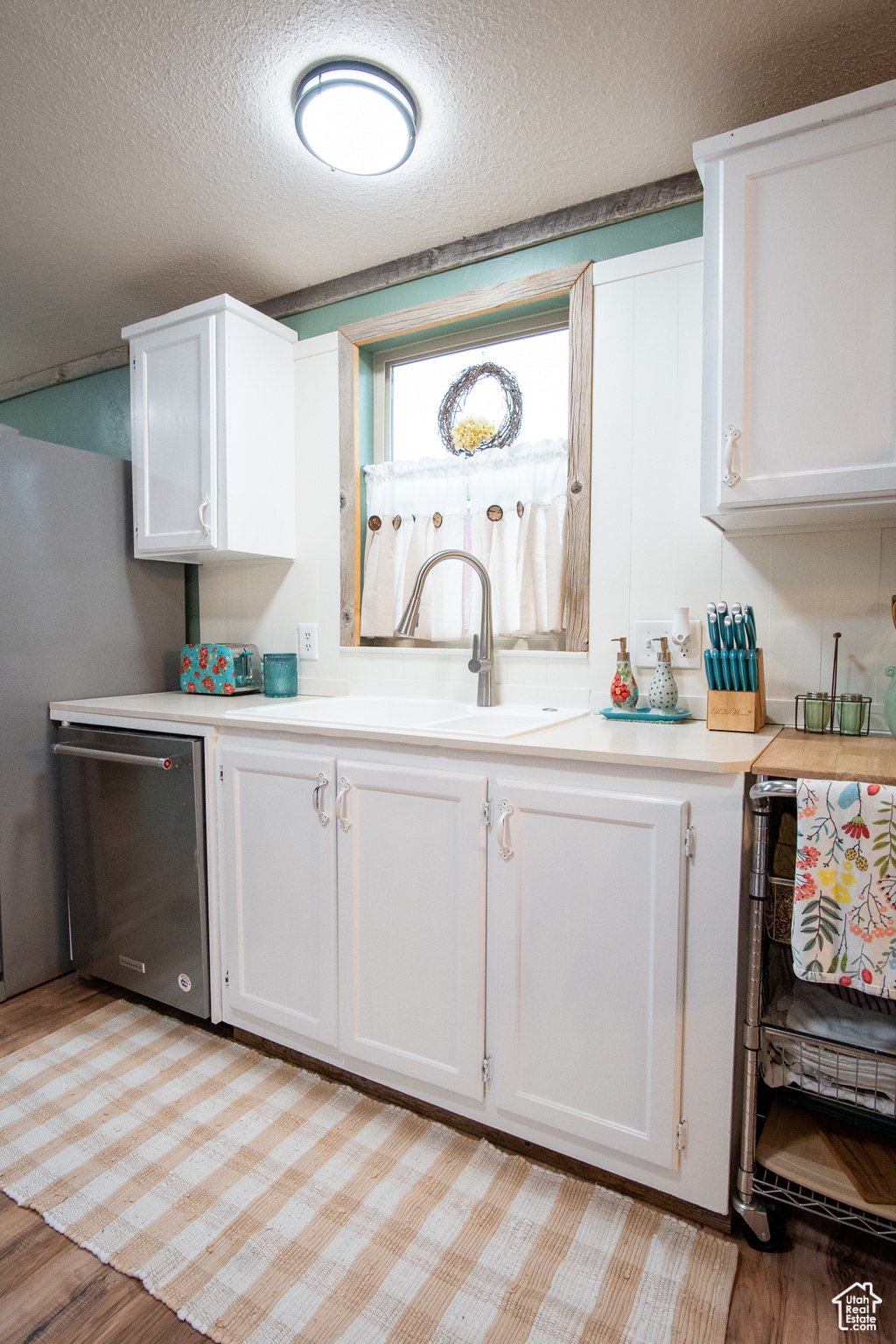 Kitchen featuring dishwasher, sink, white cabinets, and a textured ceiling