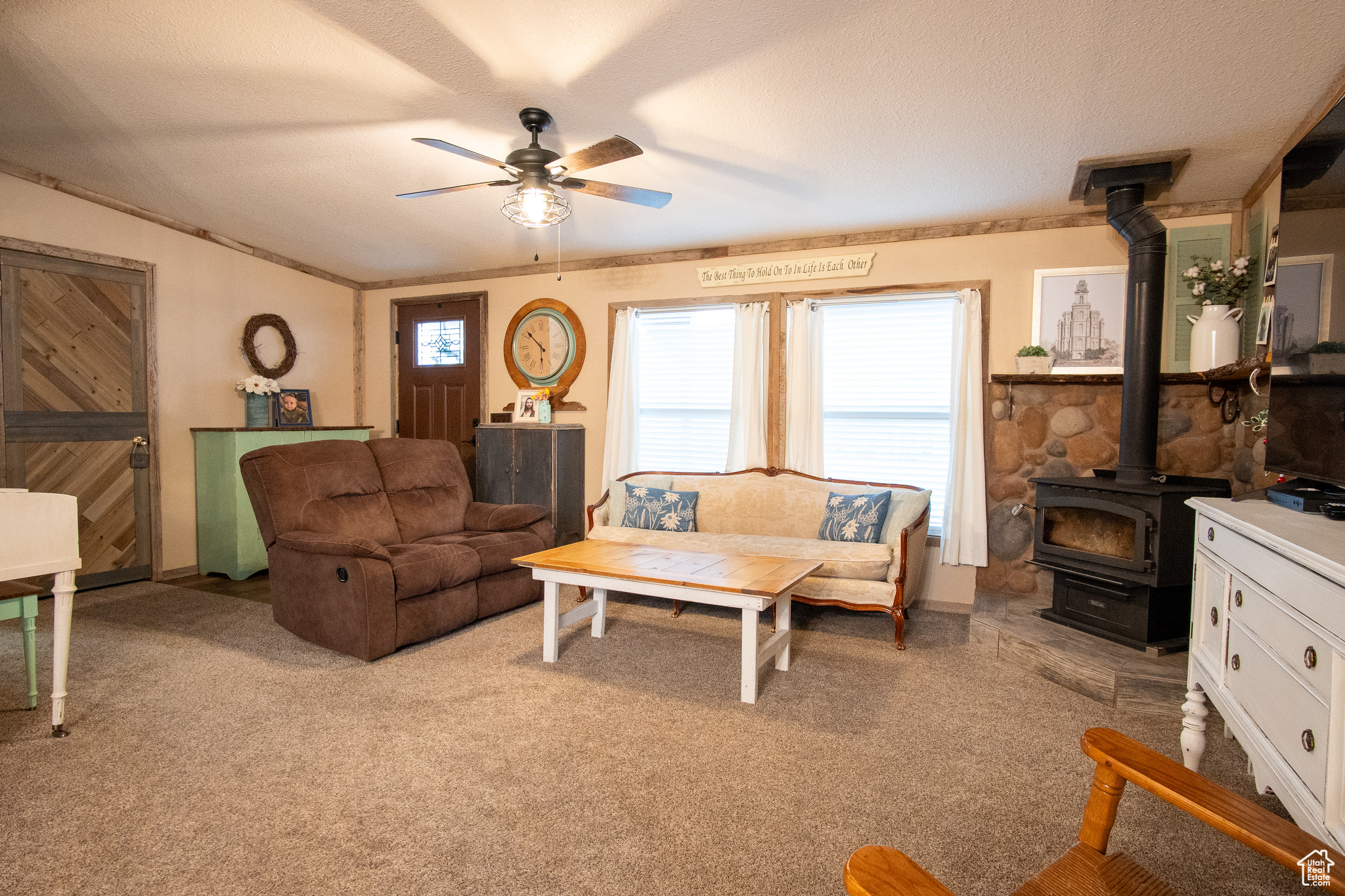 Living room with ceiling fan, light colored carpet, a textured ceiling, and a wood stove