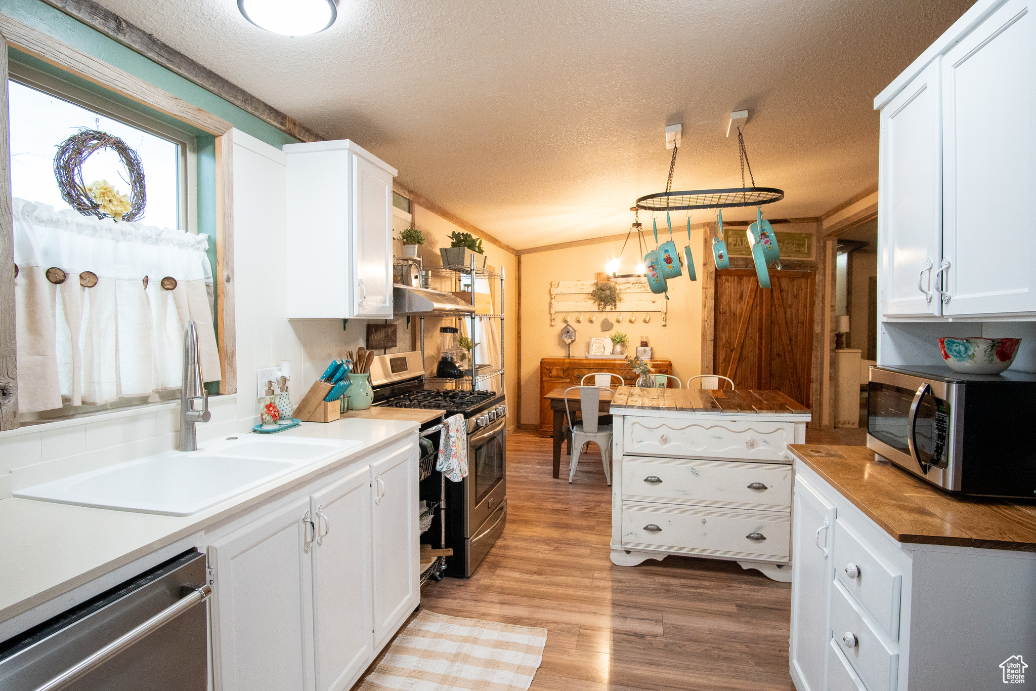 Kitchen with sink, appliances with stainless steel finishes, hanging light fixtures, a textured ceiling, and white cabinets