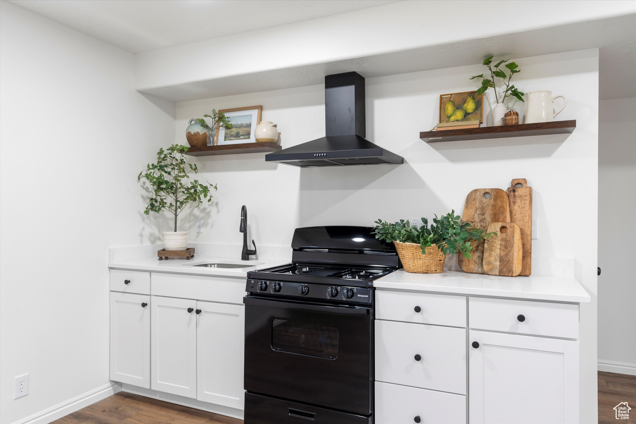 Kitchen with dark hardwood / wood-style floors, sink, white cabinets, black range with gas stovetop, and wall chimney exhaust hood