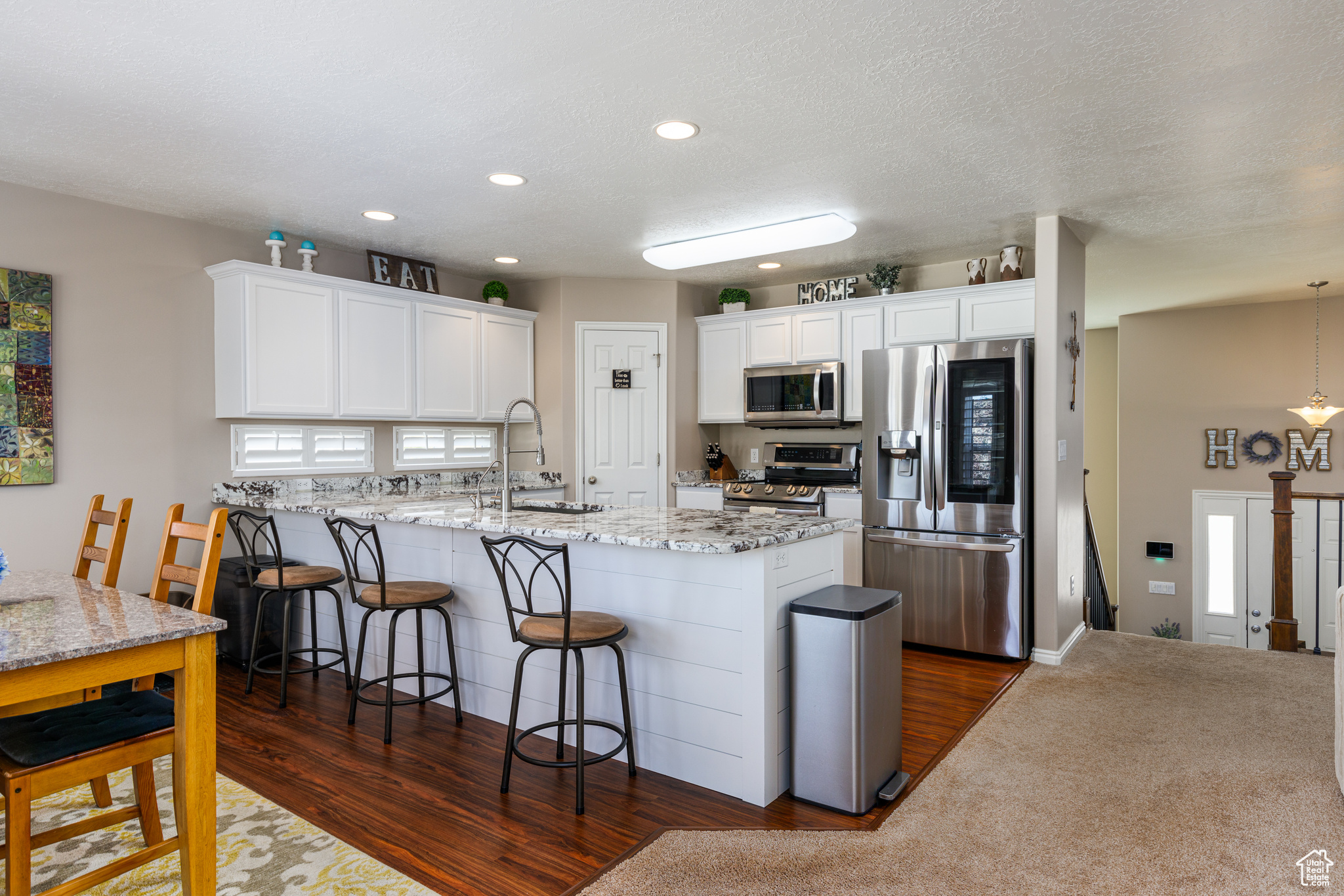 Kitchen featuring appliances with stainless steel finishes, white cabinetry, sink, kitchen peninsula, and light stone countertops