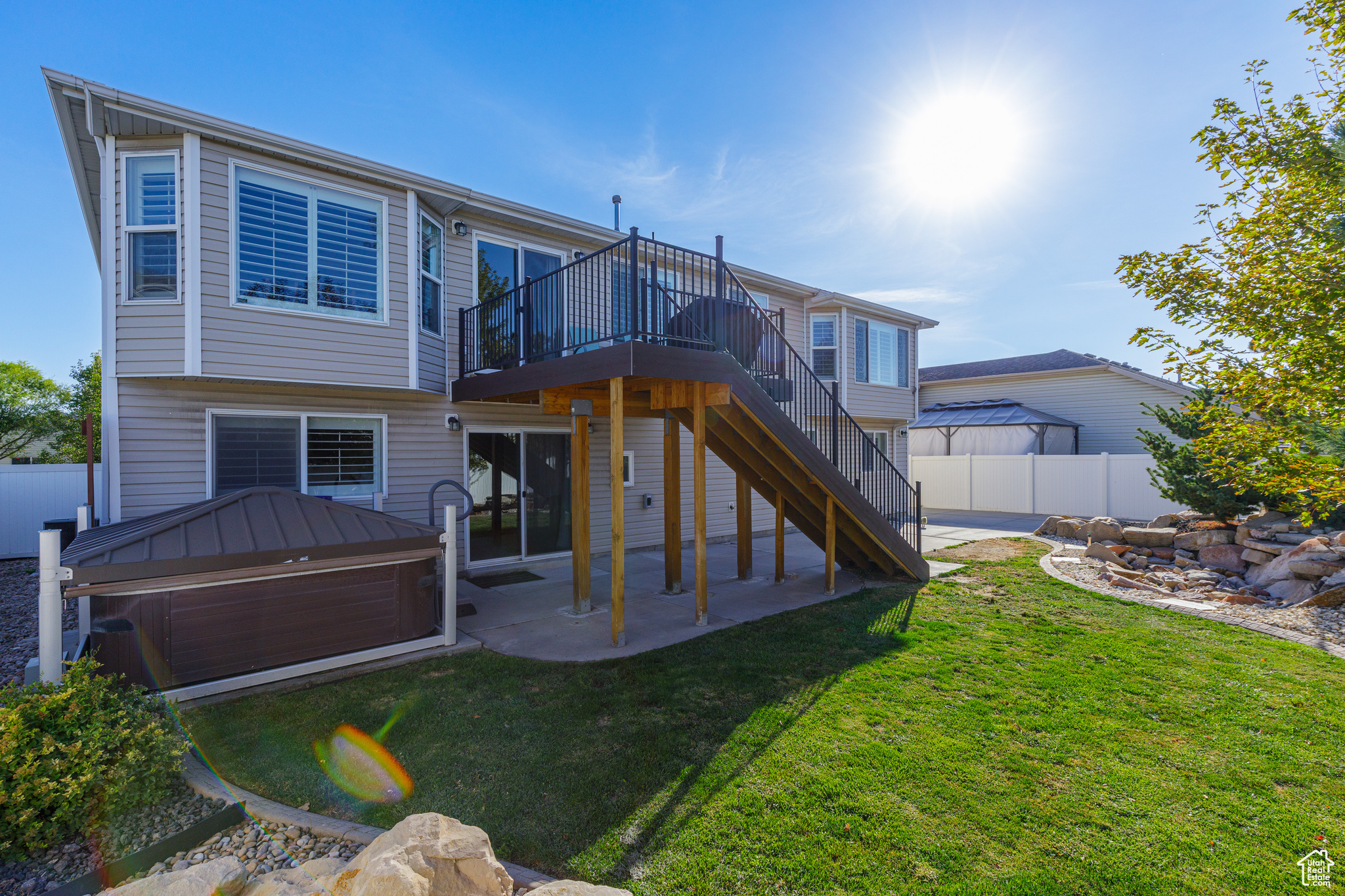 Back of property featuring a jacuzzi, a deck, a patio, and a lawn