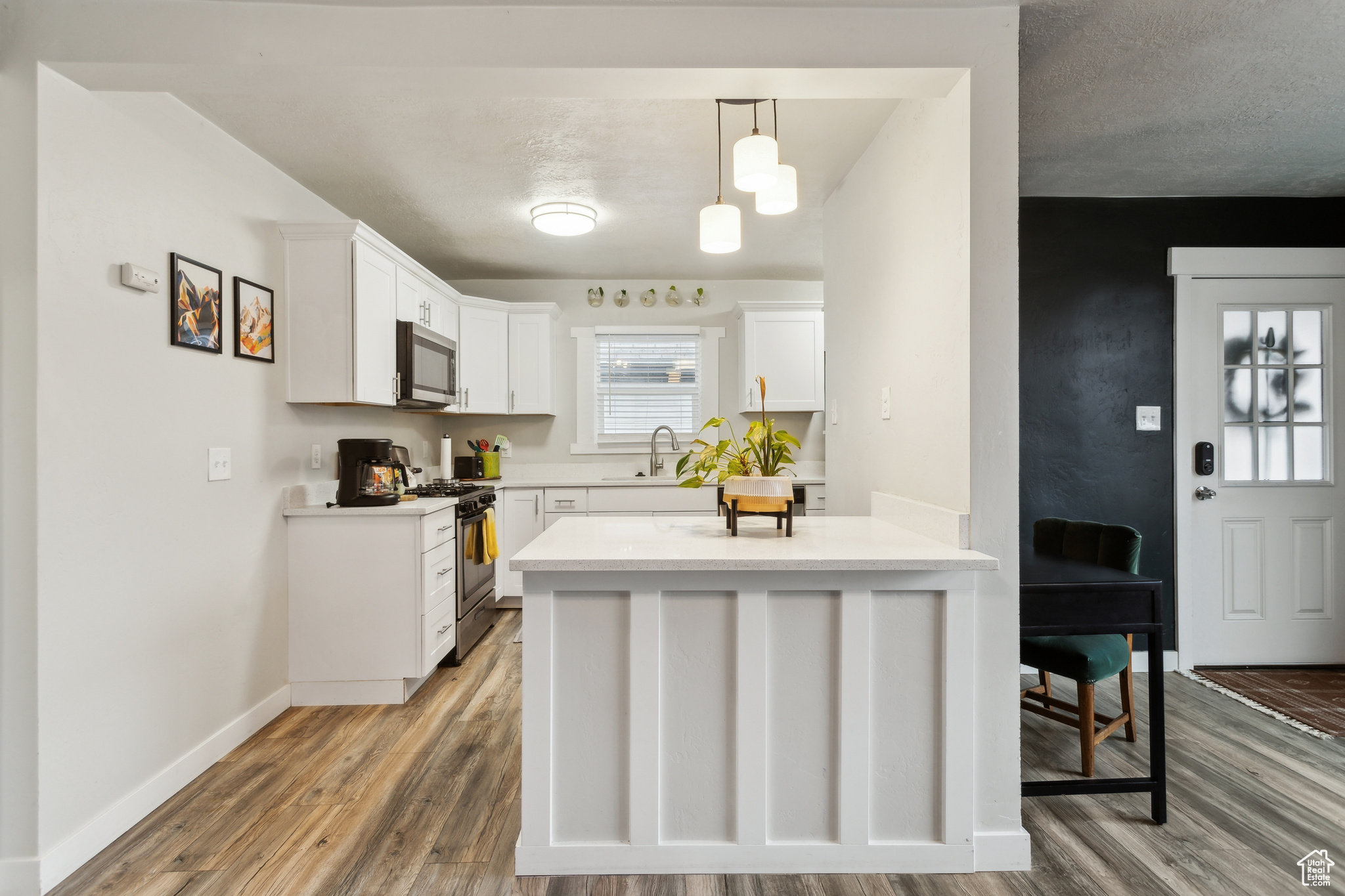 Kitchen with decorative light fixtures, white cabinetry, wood-type flooring, sink, and stainless steel appliances
