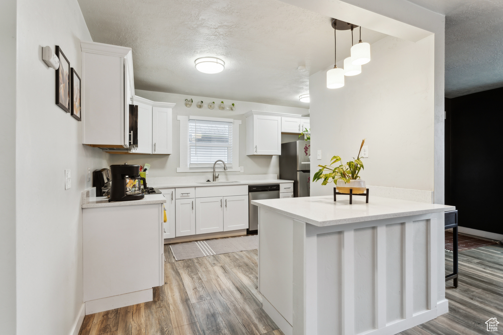 Kitchen featuring sink, white cabinets, hanging light fixtures, light hardwood / wood-style floors, and stainless steel appliances
