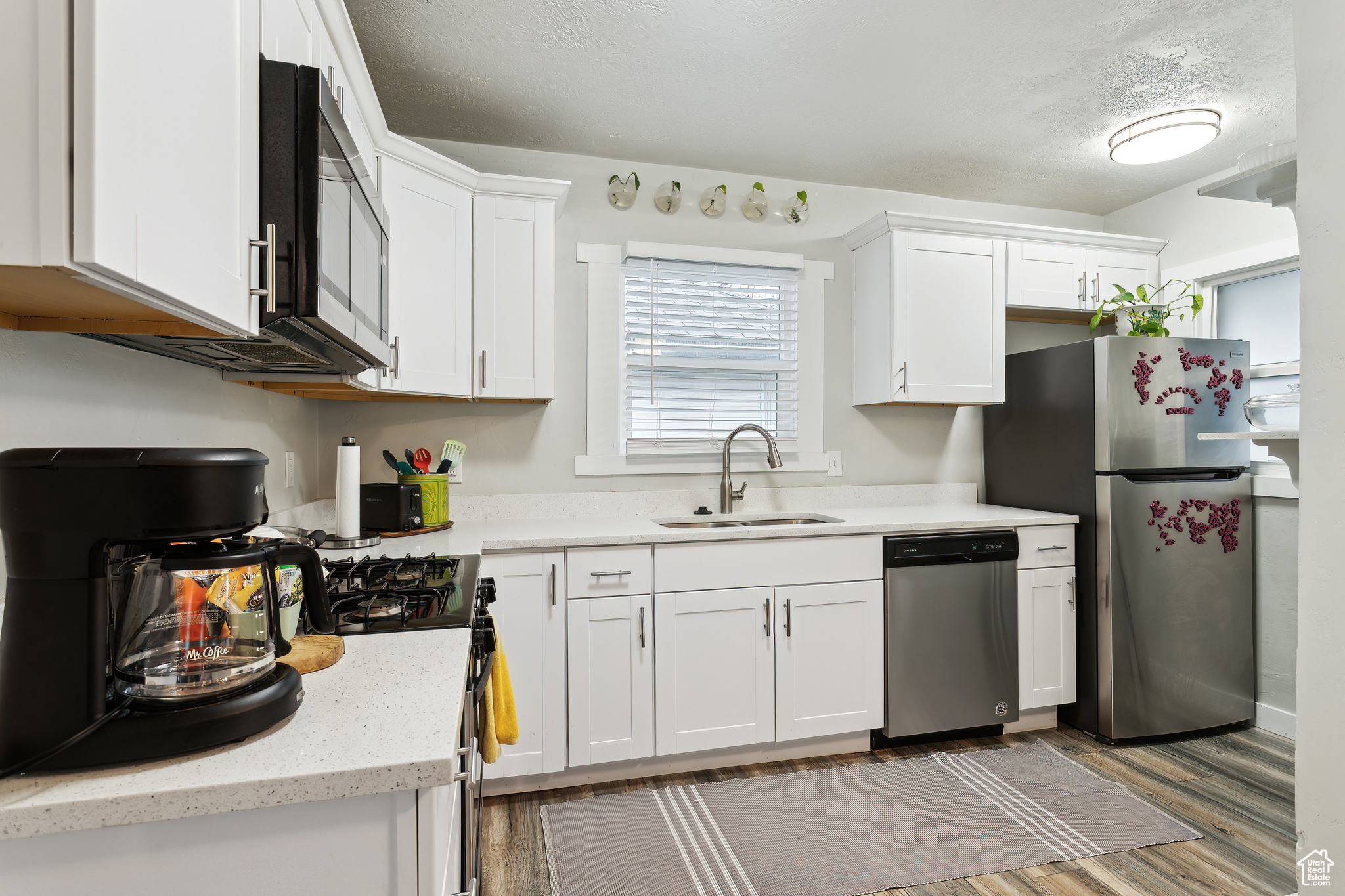 Kitchen with white cabinetry, sink, hardwood / wood-style flooring, stainless steel appliances, and a textured ceiling