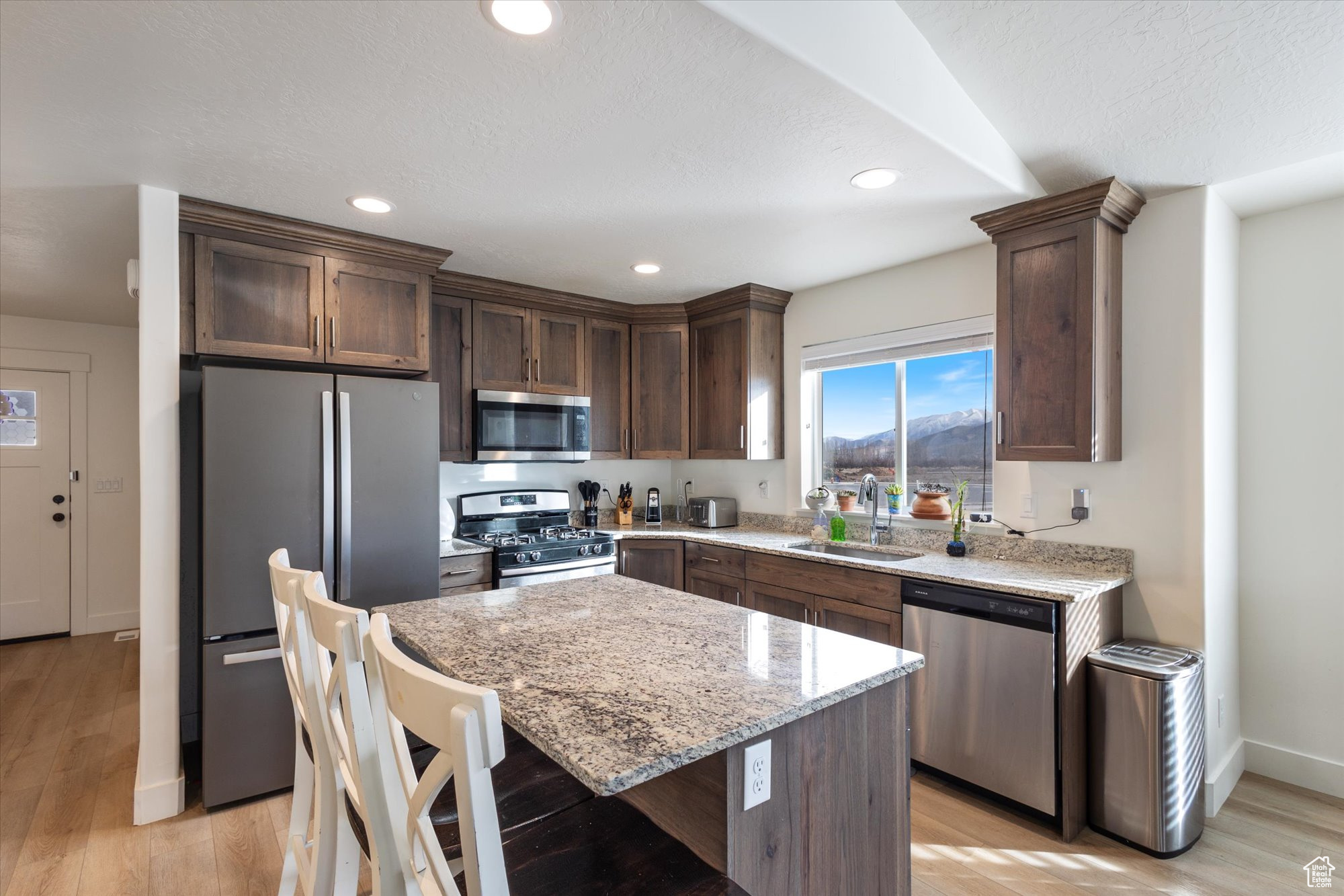 Kitchen with sink, a center island, light hardwood / wood-style flooring, appliances with stainless steel finishes, and light stone countertops