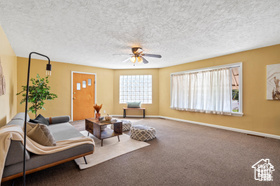 Carpeted living room featuring ceiling fan and a textured ceiling