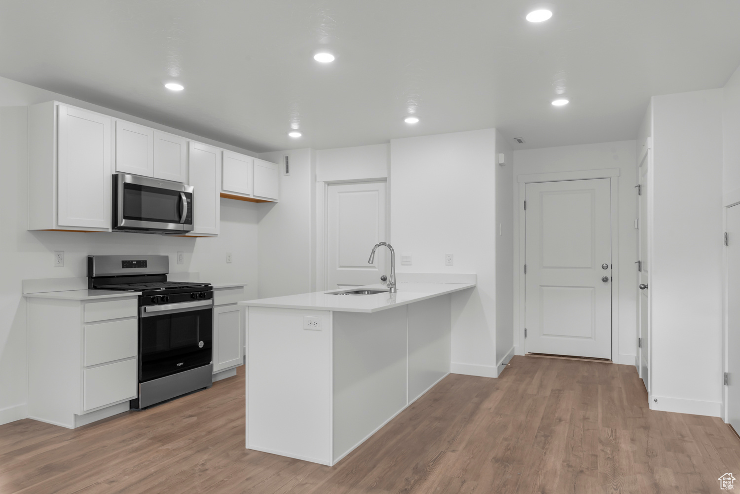 Kitchen with sink, white cabinets, kitchen peninsula, stainless steel appliances, and light hardwood / wood-style flooring