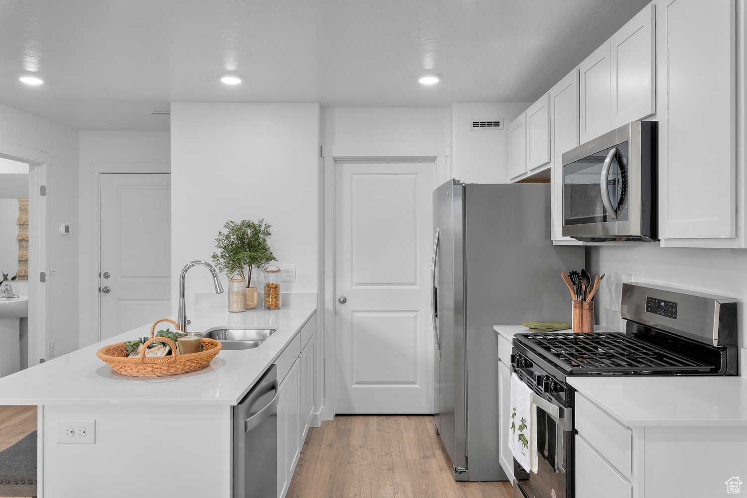 Kitchen with white cabinetry, sink, stainless steel appliances, and light hardwood / wood-style floors