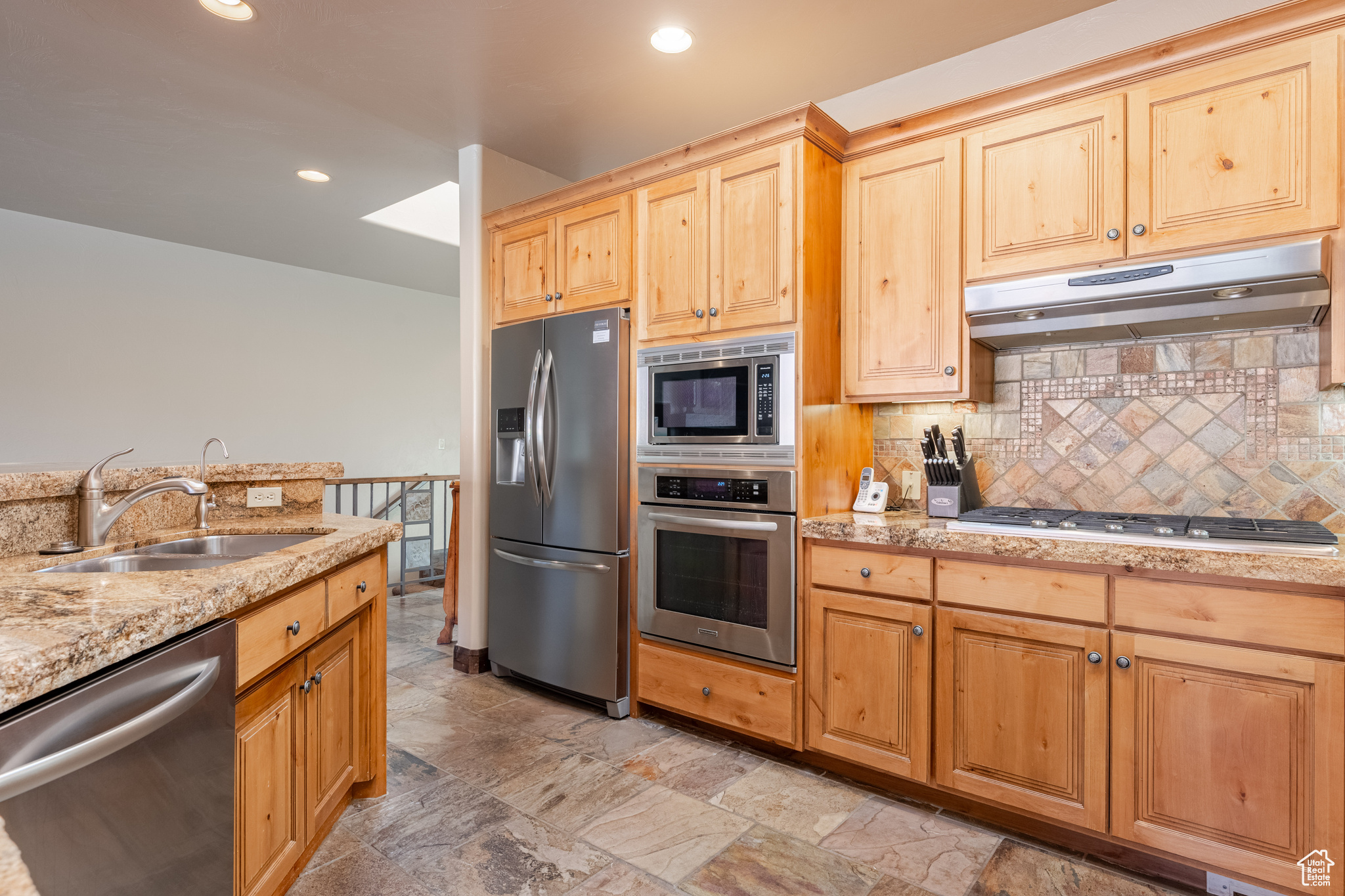 Kitchen featuring stainless steel appliances, light stone countertops, sink, and backsplash