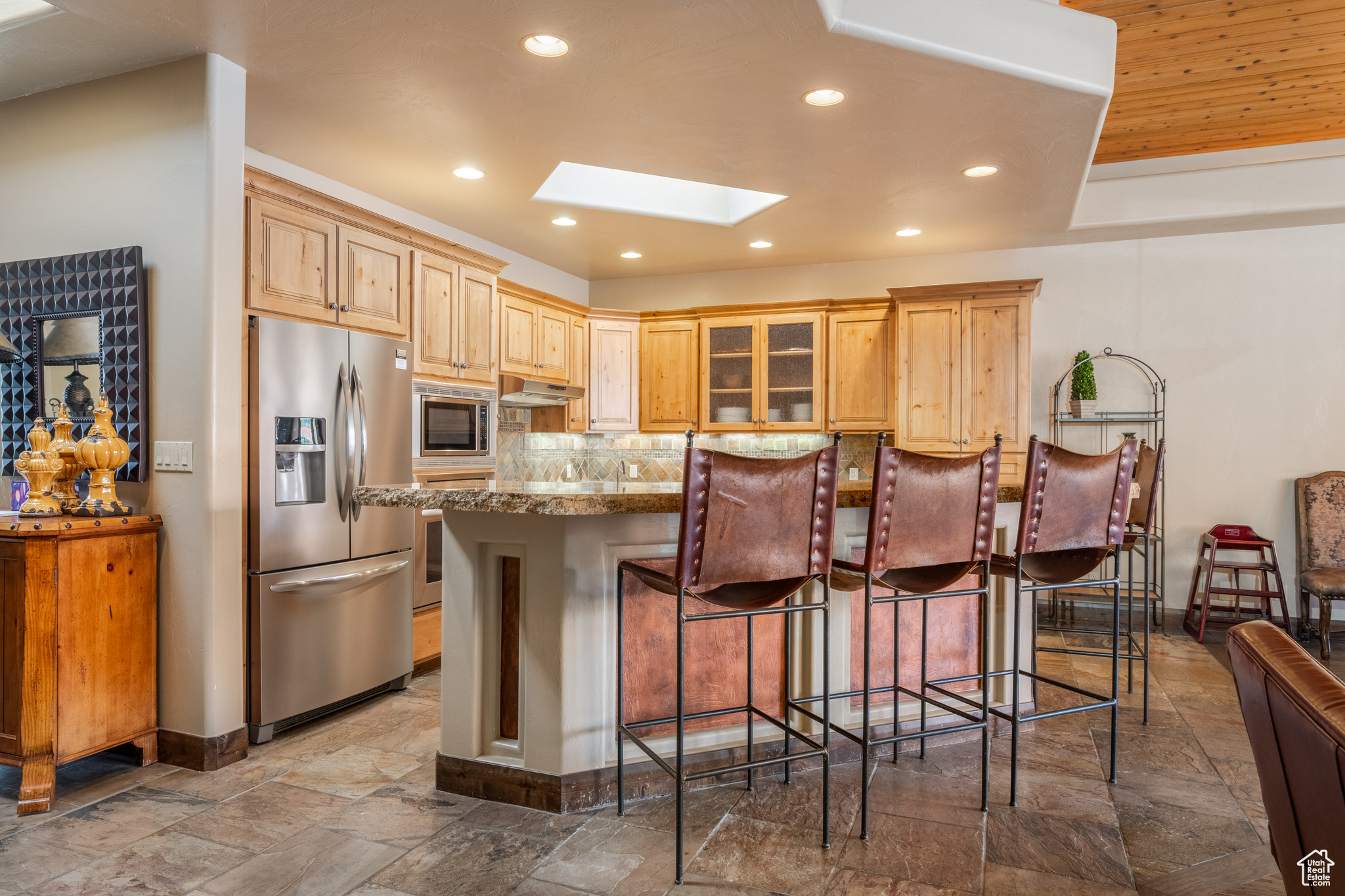 Kitchen featuring a breakfast bar, a skylight, stainless steel appliances, light stone counters, and tasteful backsplash
