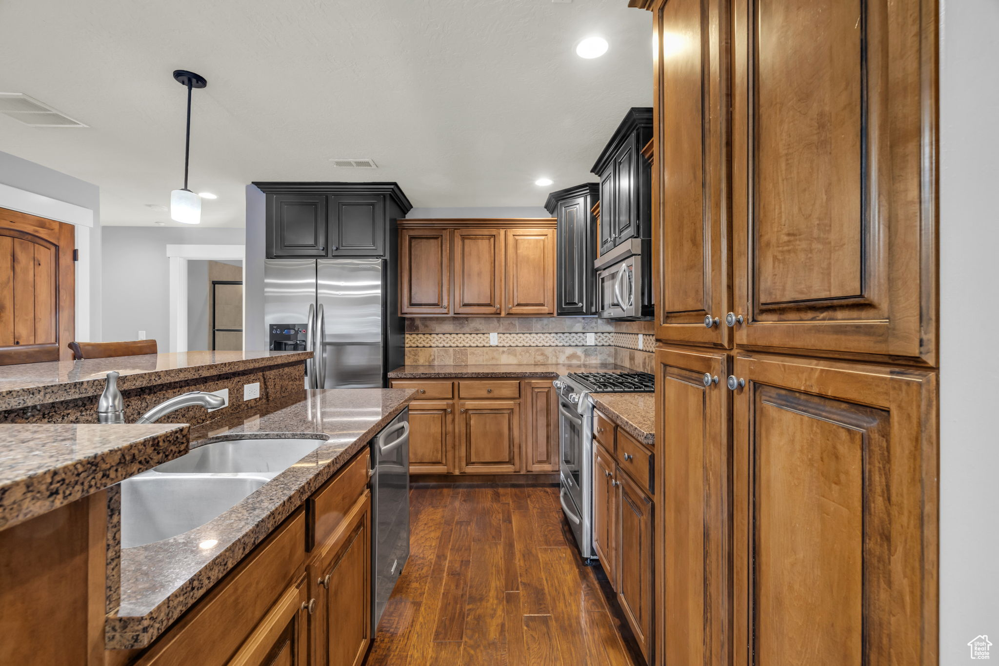 Kitchen with sink, hanging light fixtures, appliances with stainless steel finishes, dark hardwood / wood-style flooring, and decorative backsplash
