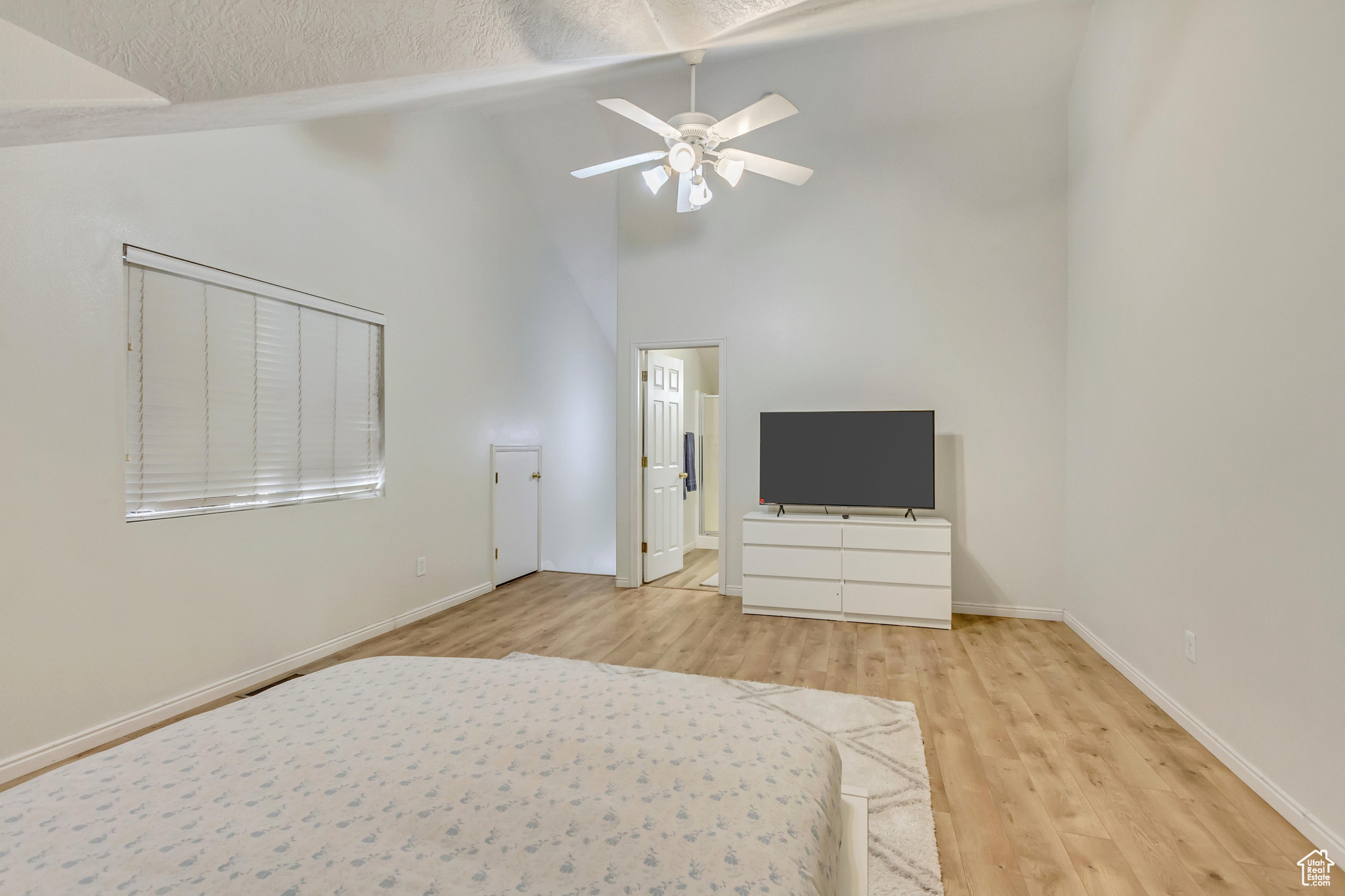 Unfurnished bedroom featuring ceiling fan, high vaulted ceiling, a textured ceiling, and light hardwood / wood-style floors