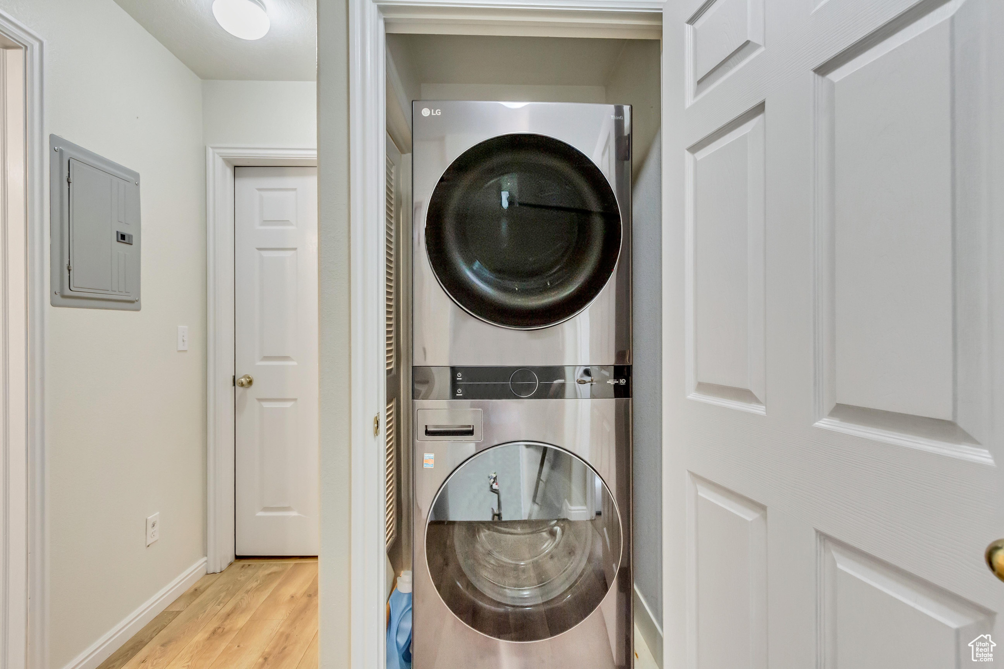 Washroom with stacked washer and dryer, light hardwood / wood-style flooring, and electric panel