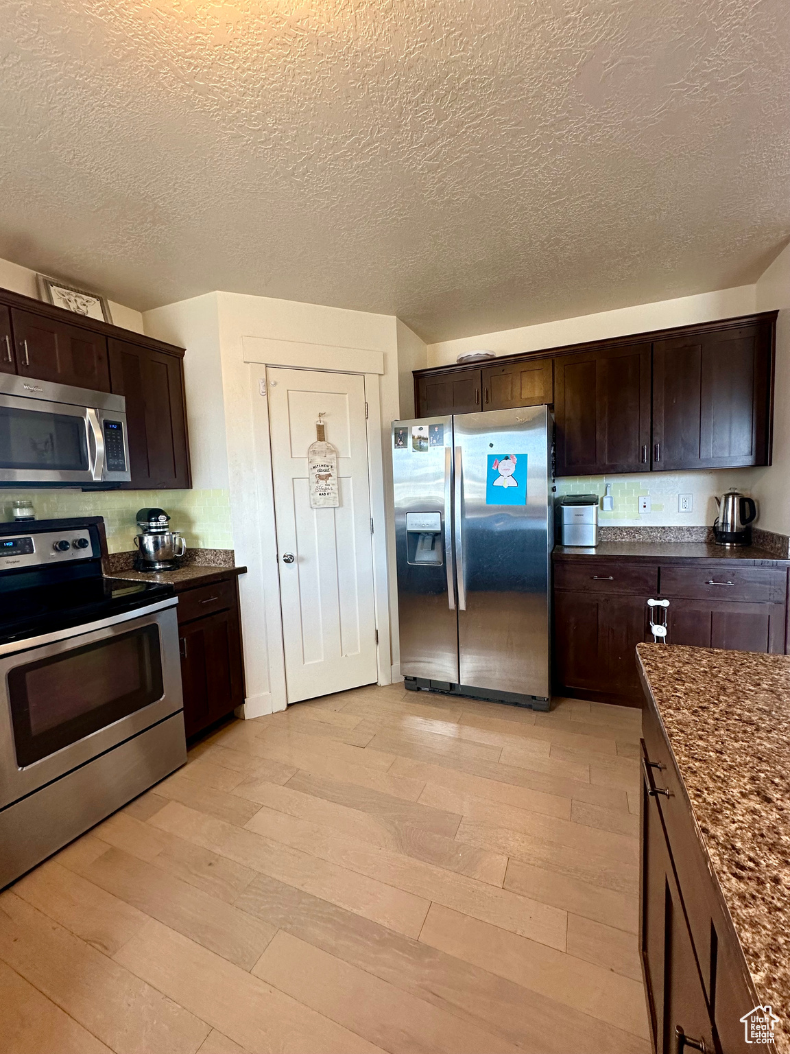 Kitchen featuring appliances with stainless steel finishes, dark brown cabinets, dark stone countertops, and light hardwood / wood-style flooring