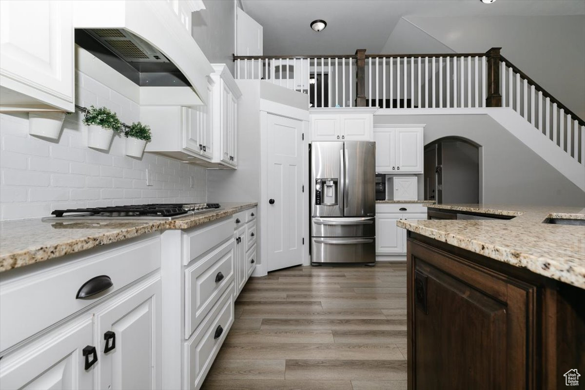 Kitchen with white cabinetry, appliances with stainless steel finishes, light stone countertops, and hardwood / wood-style floors