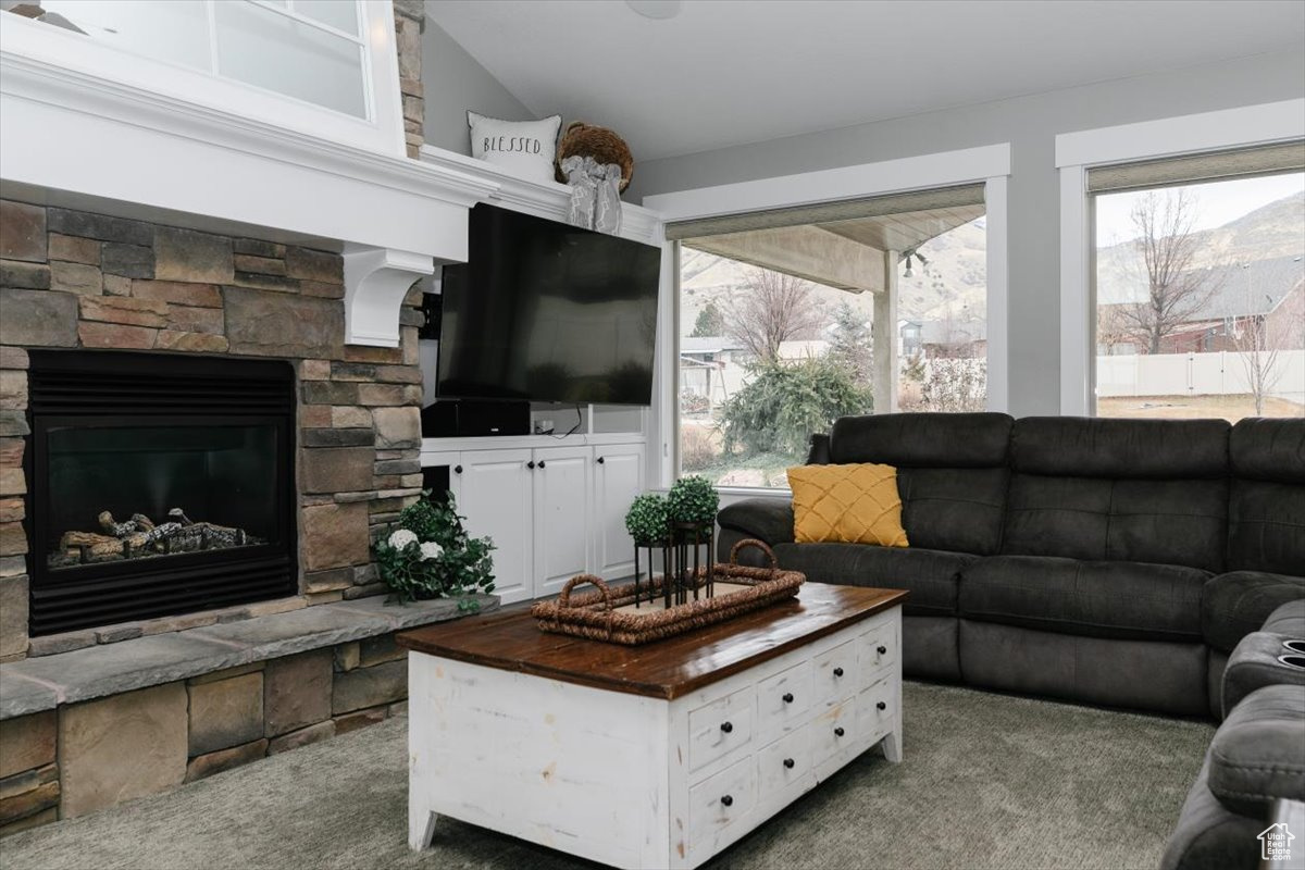 Carpeted living room with lofted ceiling and a stone fireplace