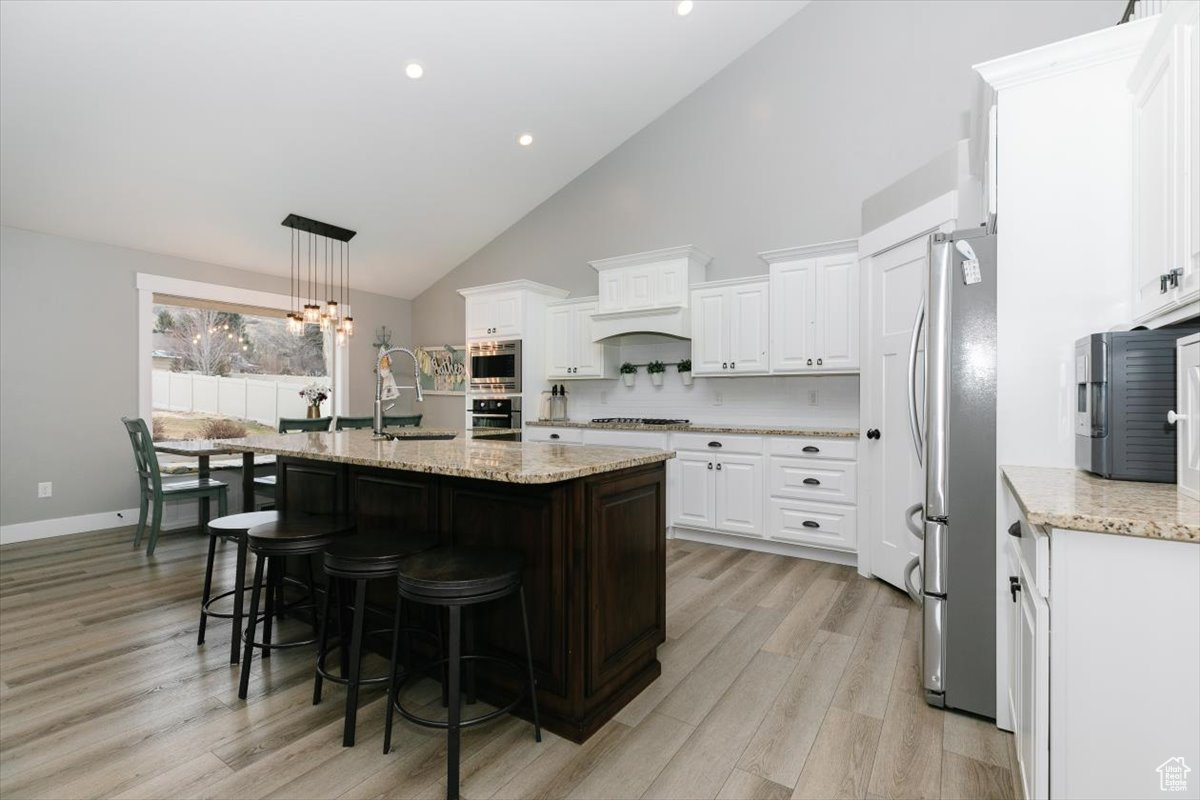 Kitchen with sink, stainless steel appliances, an island with sink, white cabinets, and decorative light fixtures