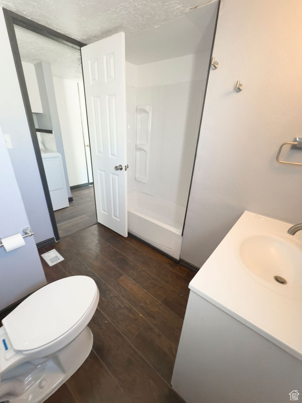Bathroom featuring washer / clothes dryer, hardwood / wood-style flooring, vanity, toilet, and a textured ceiling