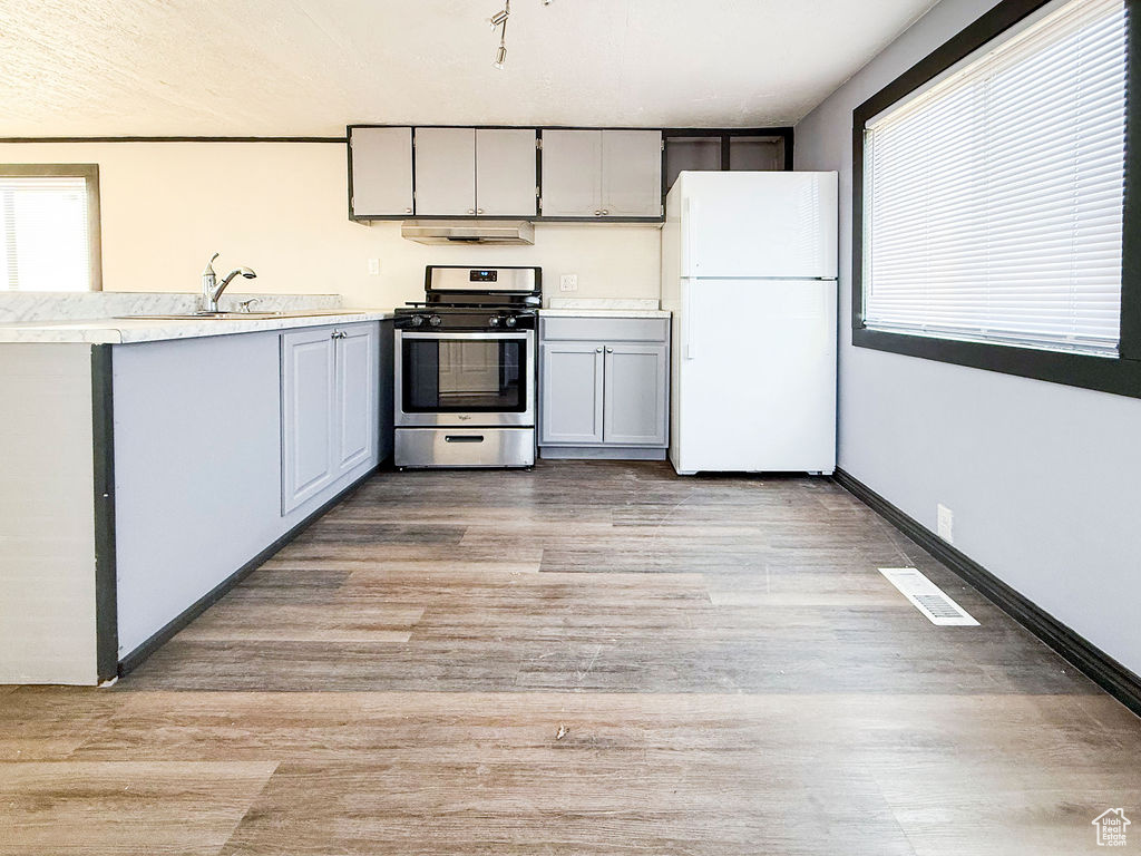 Kitchen with white refrigerator, gray cabinetry, light hardwood / wood-style floors, and stainless steel gas stove