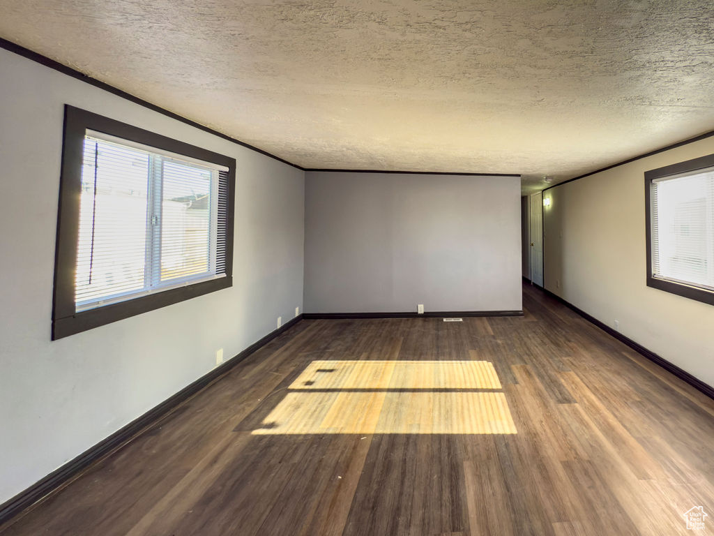 Empty room with ornamental molding, dark hardwood / wood-style floors, and a textured ceiling