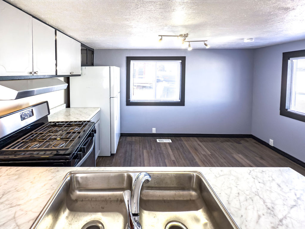 Kitchen with dark wood-type flooring, white cabinetry, a textured ceiling, stainless steel range with gas stovetop, and exhaust hood