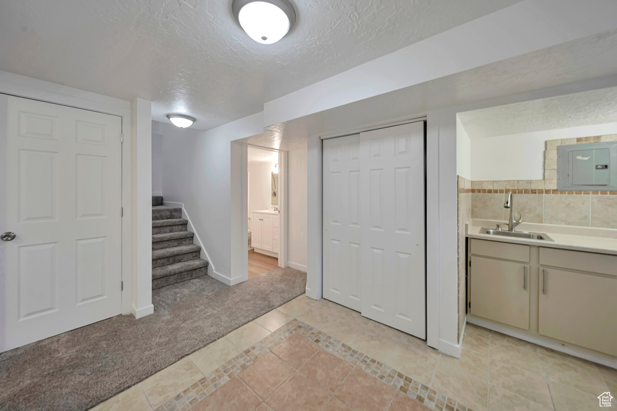Basement with sink, light colored carpet, electric panel, and a textured ceiling