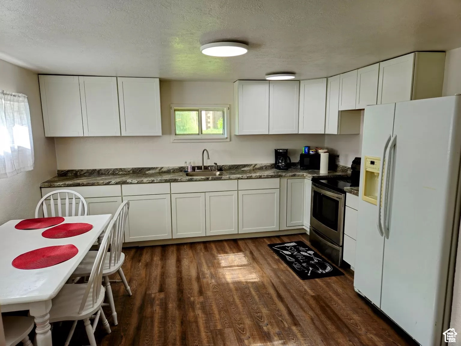 Kitchen featuring white cabinetry, stainless steel electric stove, and white refrigerator with ice dispenser